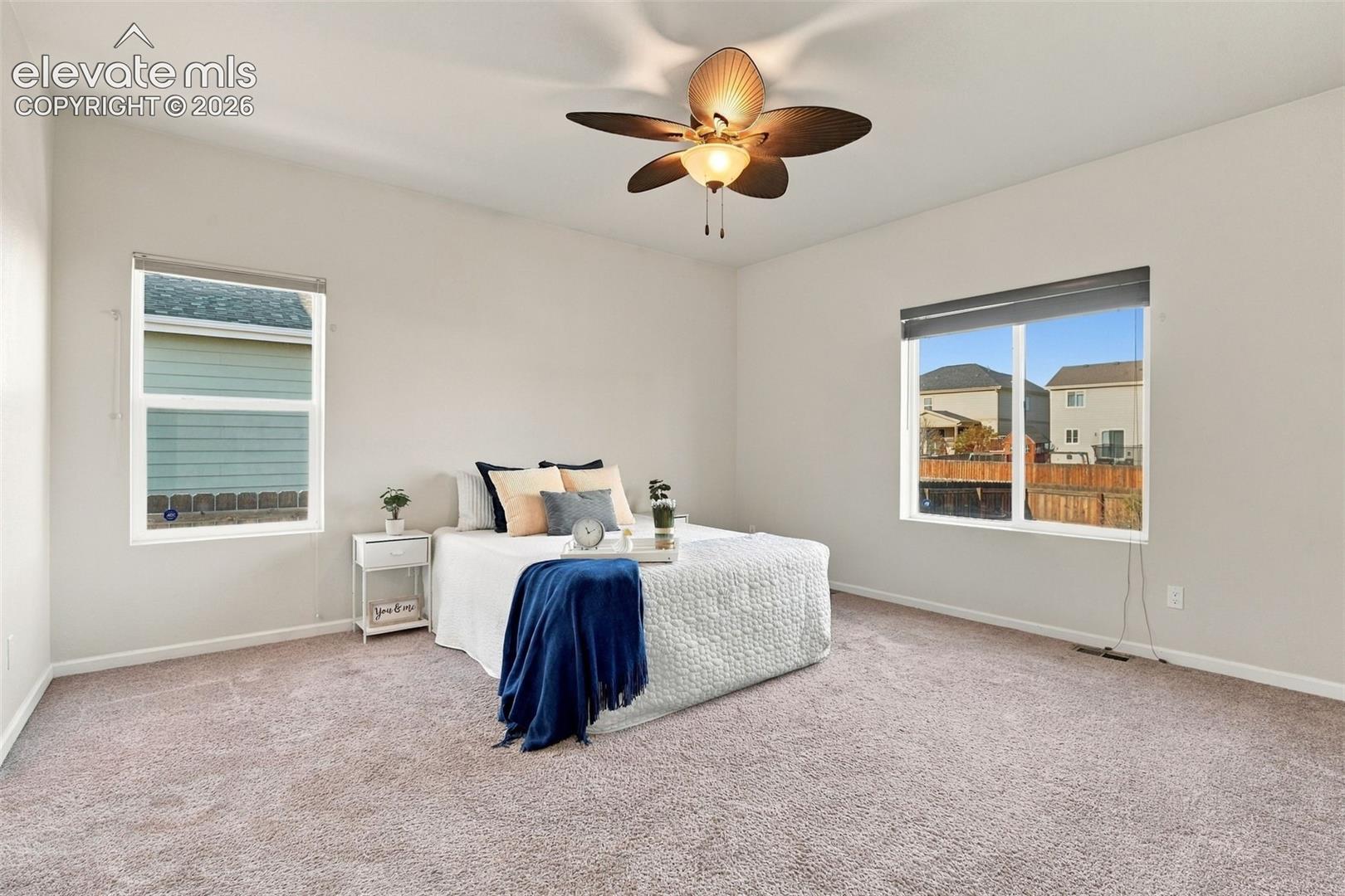 Neutral-toned bedroom featuring carpeting, dual windows, and a multi-blade ceiling fan with integrated lighting
