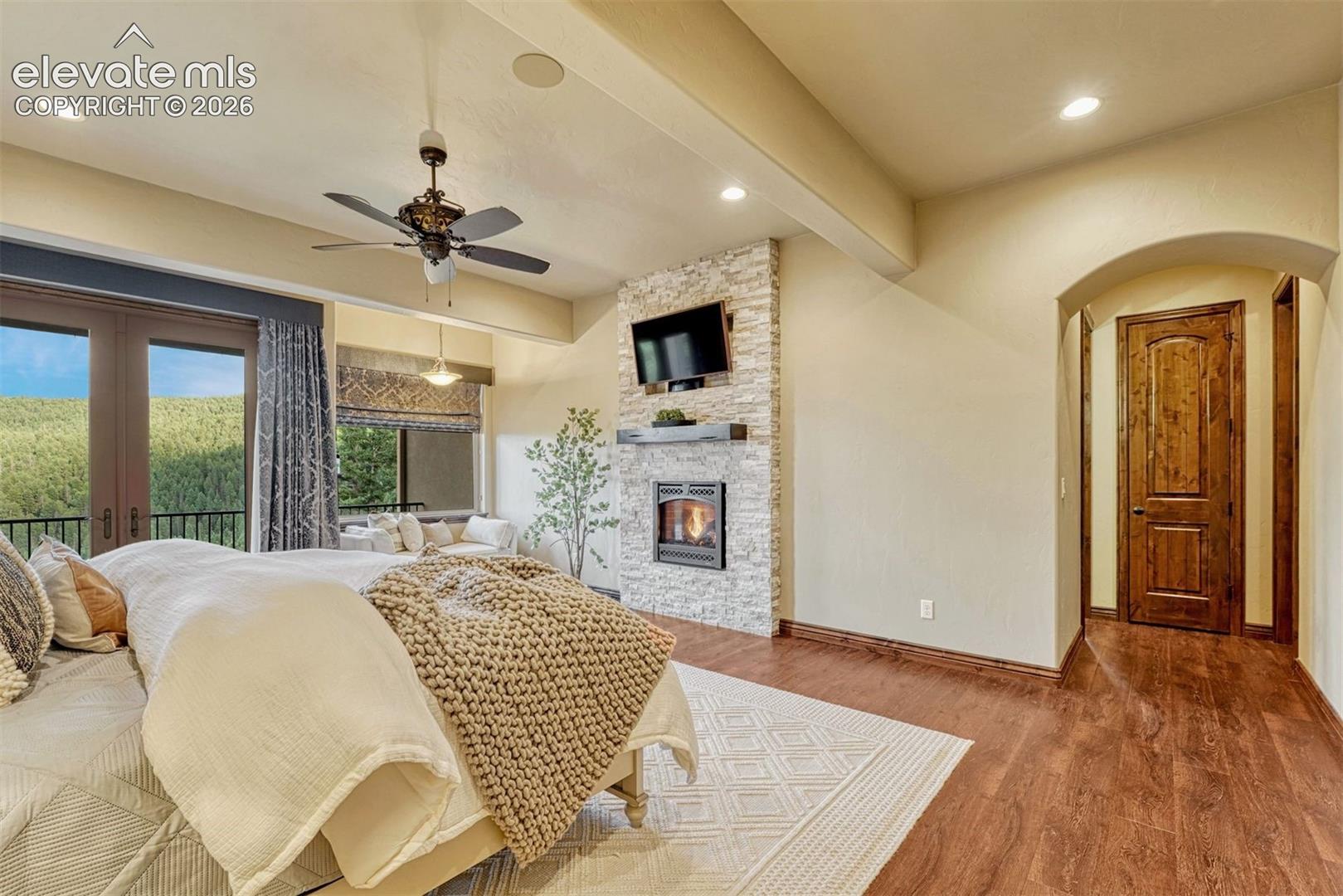 Wood-finish flooring, stone-clad fireplace, French doors, ceiling fan, and recessed lighting