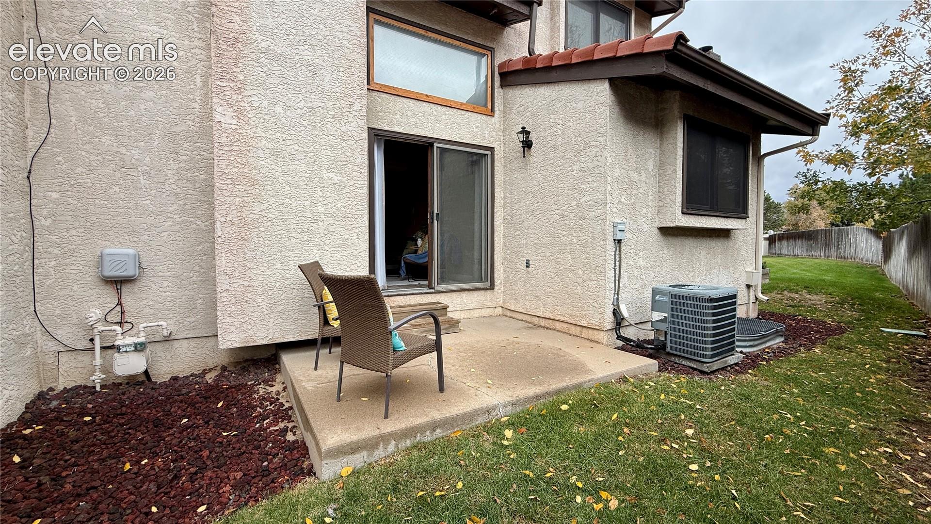 Stucco exterior featuring a concrete patio, sliding glass door, fixed upper window, and terracotta-style roof accents
