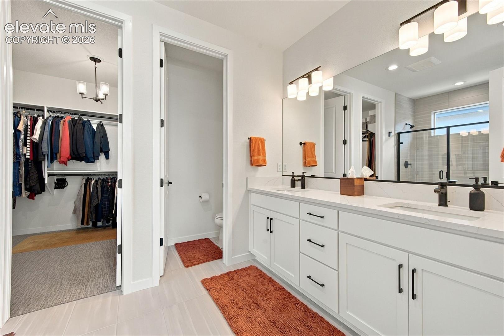 Double vanity with quartz countertop, white shaker-style cabinetry, matte black hardware, dual undermount sinks, and wall-to-wall mirror with multi-light fixture