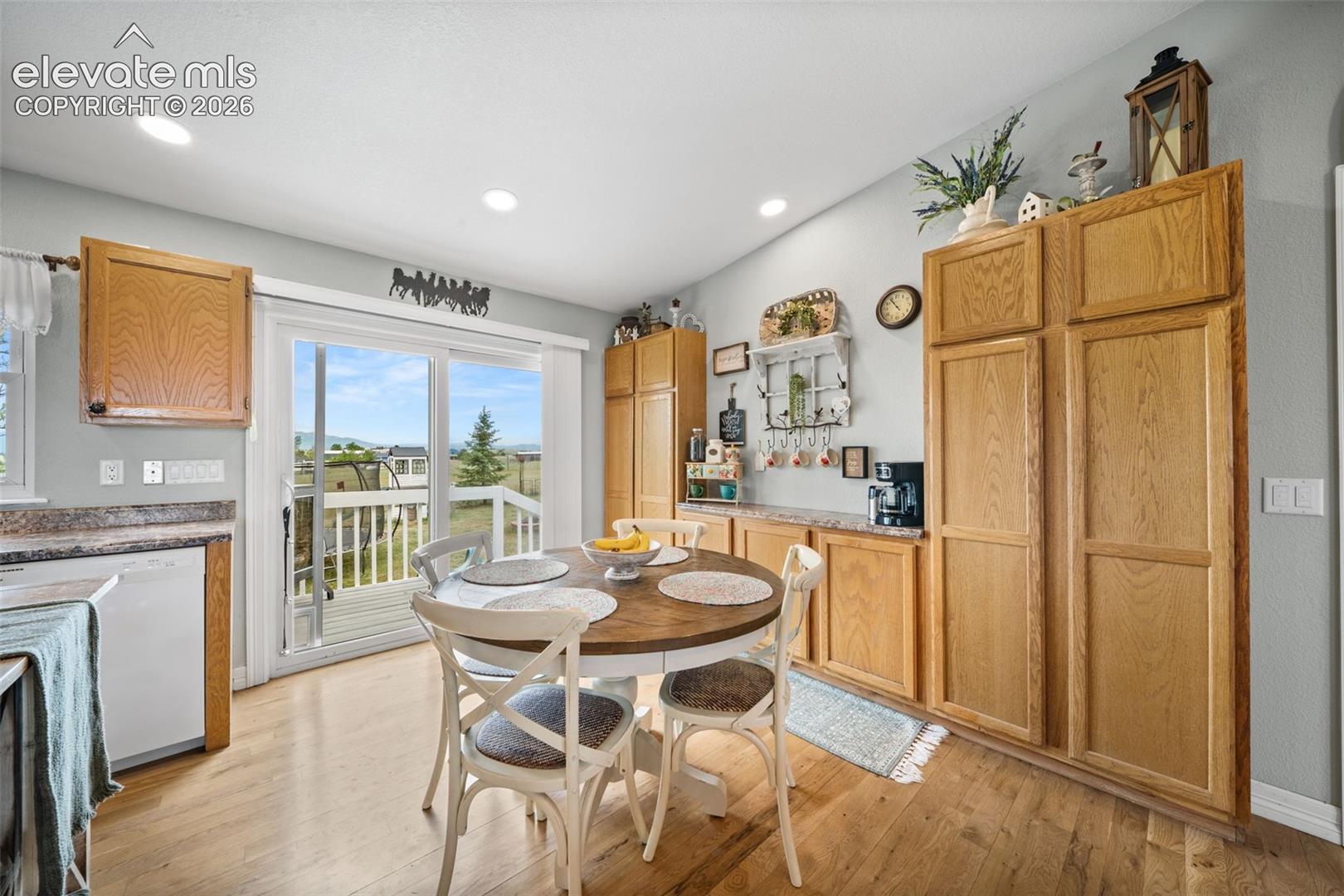Kitchen dining area featuring wood-finish flooring, light wood cabinetry, recessed lighting, and a sliding glass door opening to an outdoor deck with railing