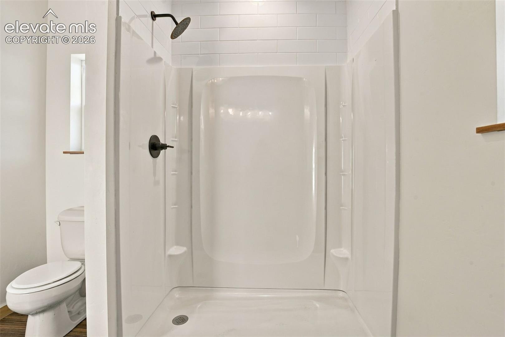 Full-height shower surround with a white subway tile accent wall, matte black shower head, and matte black handle fixture