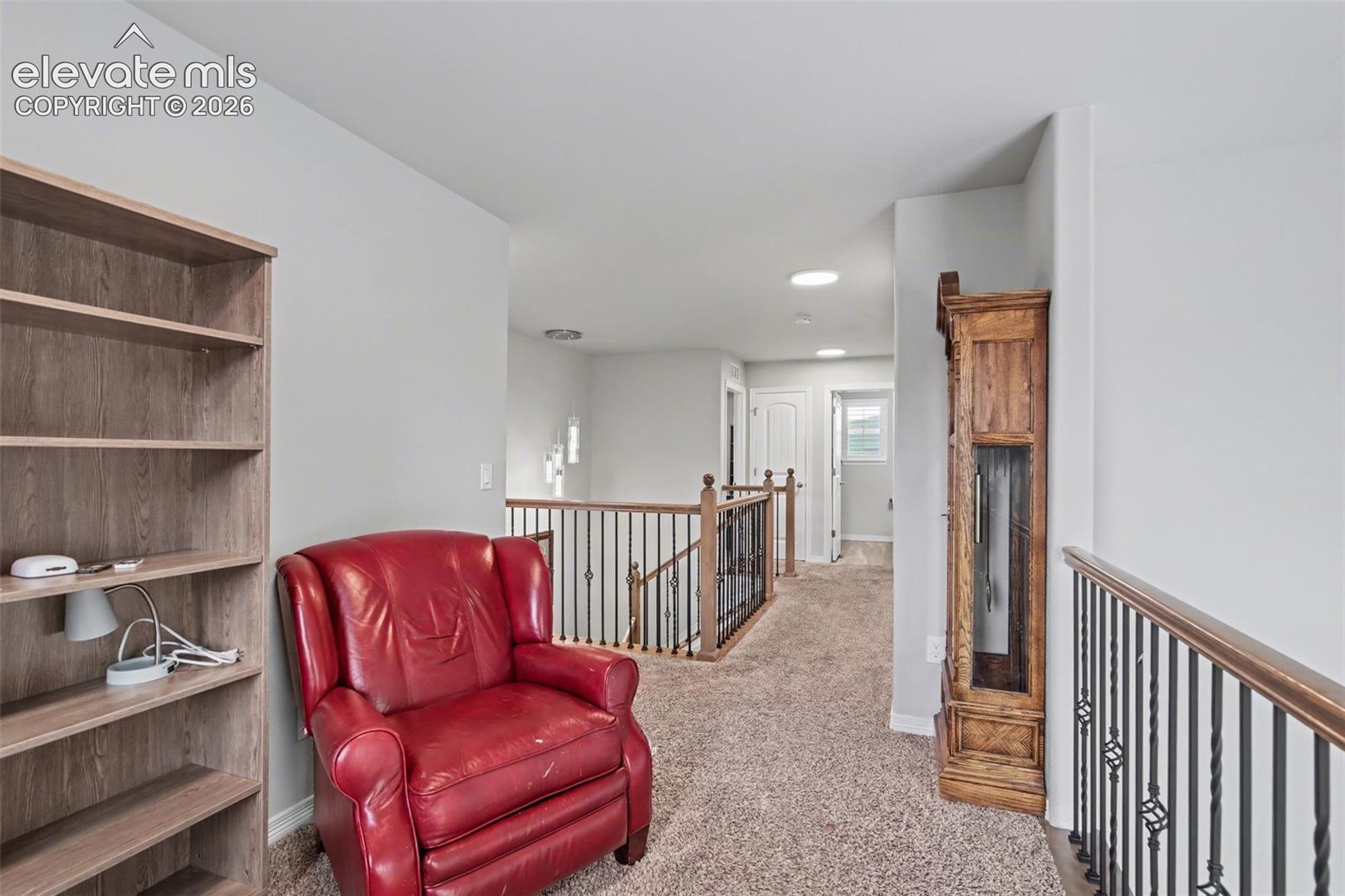 Upper-level landing featuring carpet flooring, railing with wood-finish top and wrought iron spindles, and recessed lighting
