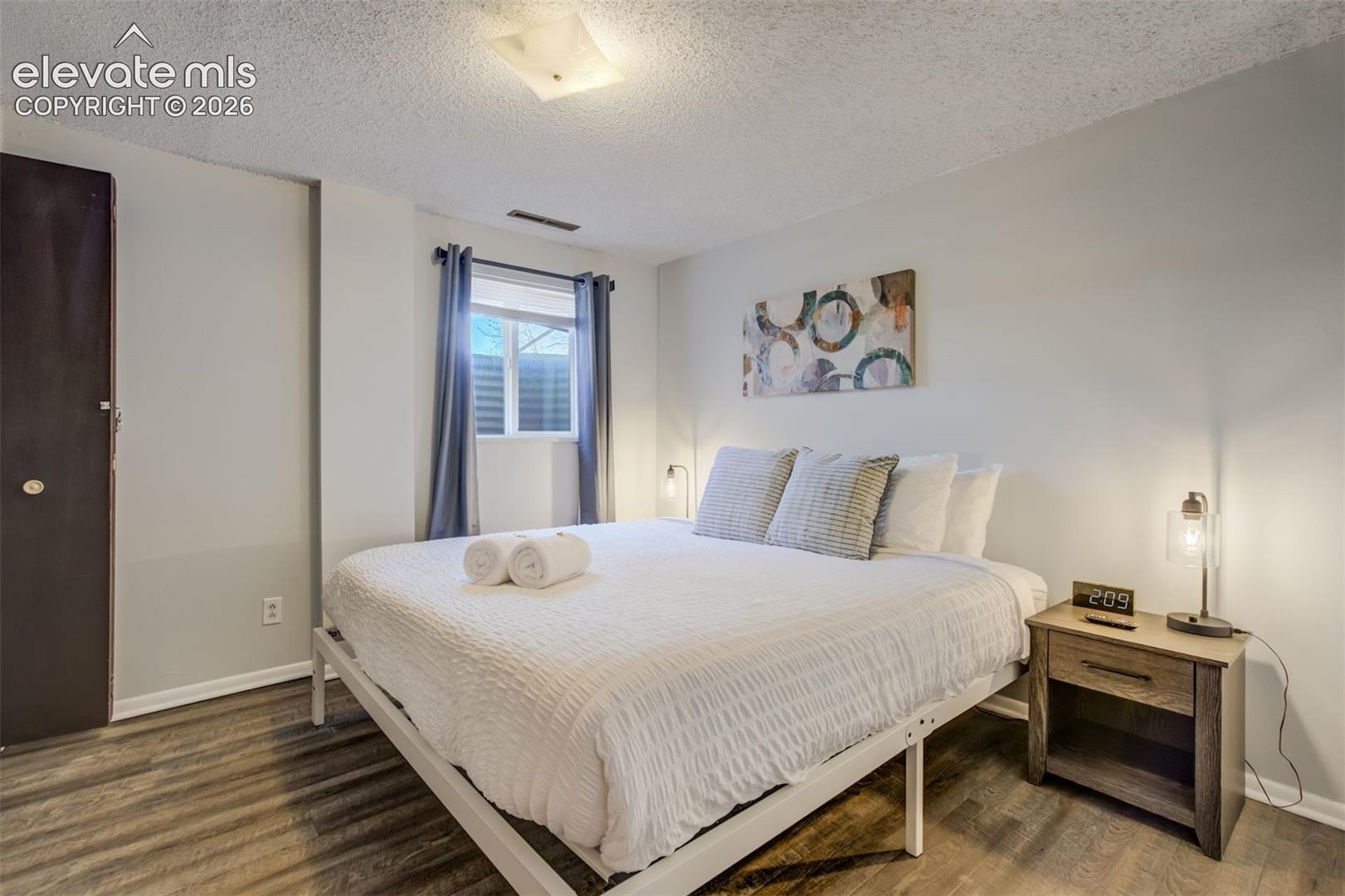 Wood-finish flooring, white walls, and a window with blinds and curtains