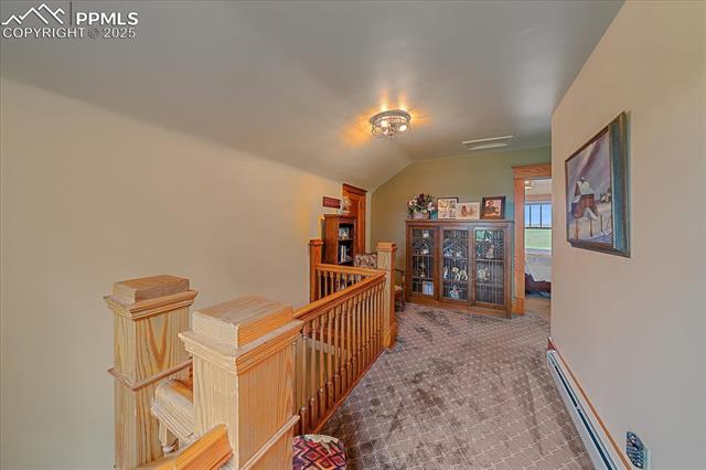 Corridor featuring an upstairs landing, a baseboard radiator, vaulted ceiling, and carpet