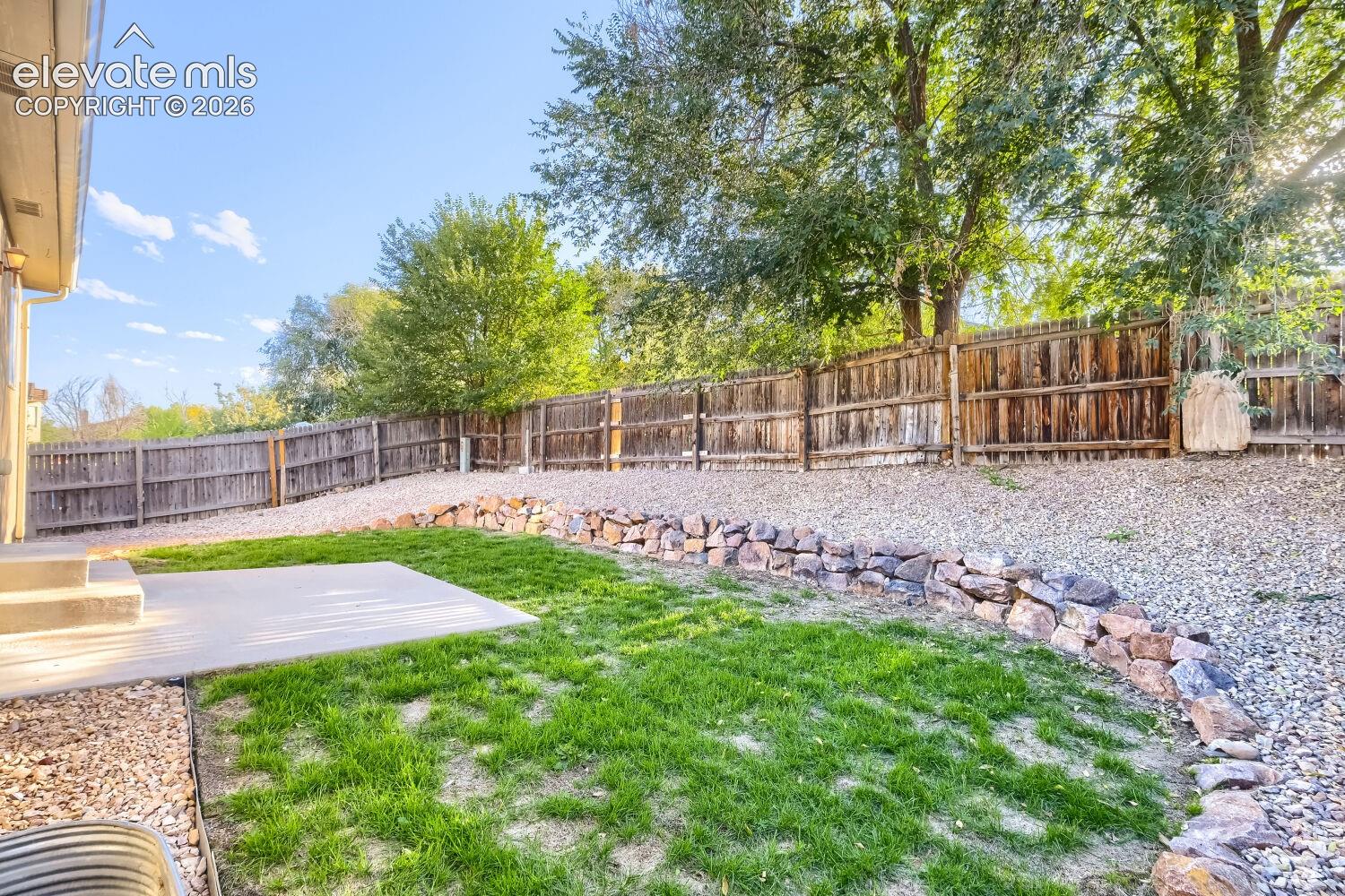 Backyard featuring a concrete patio, stone retaining wall, leveled lawn area, decorative rock landscaping, and wood privacy fencing