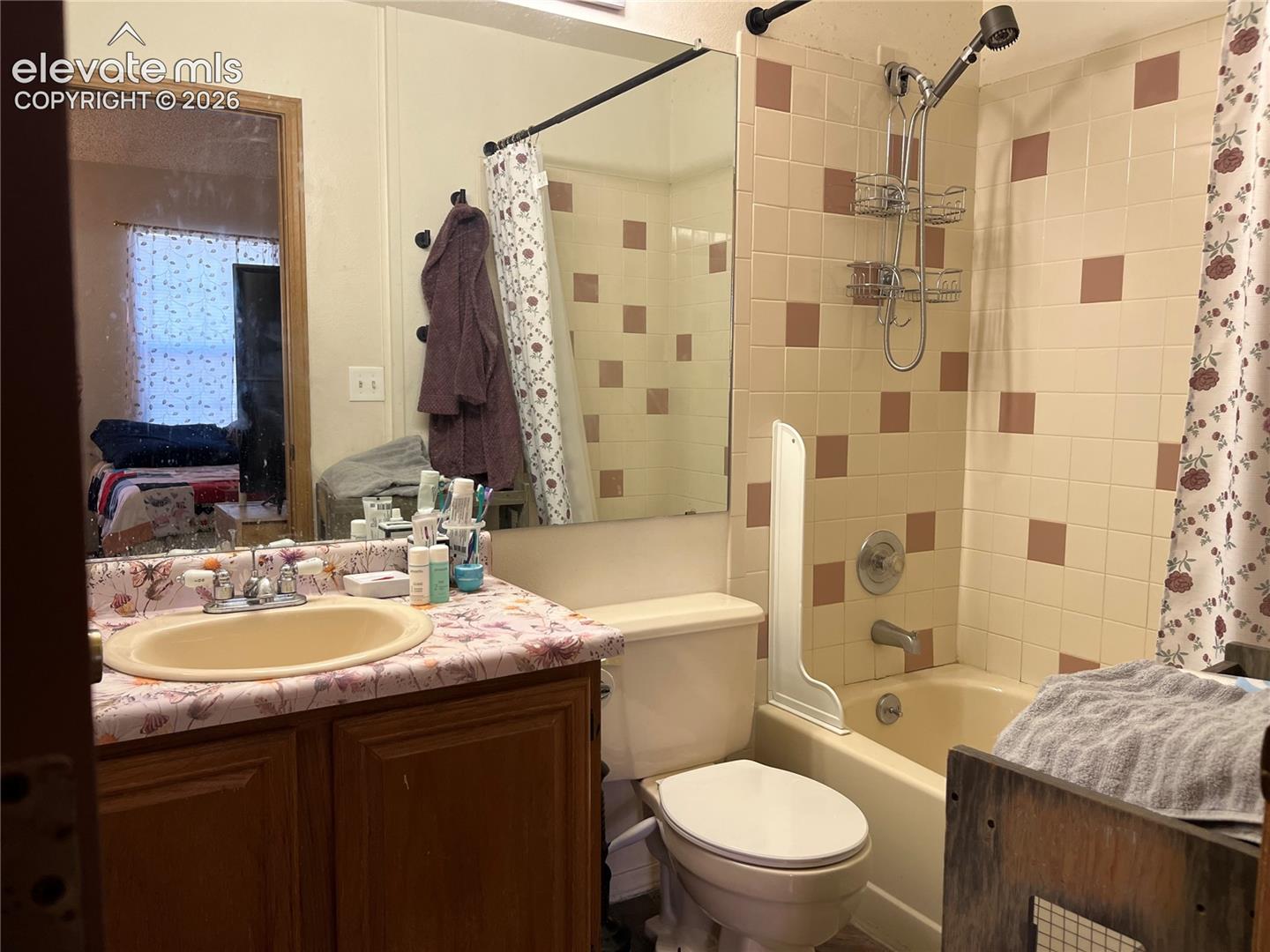 Bathroom featuring a wood-tone vanity, oval drop-in sink, expansive wall-mounted mirror, and a tub-shower combination with decorative tile surround