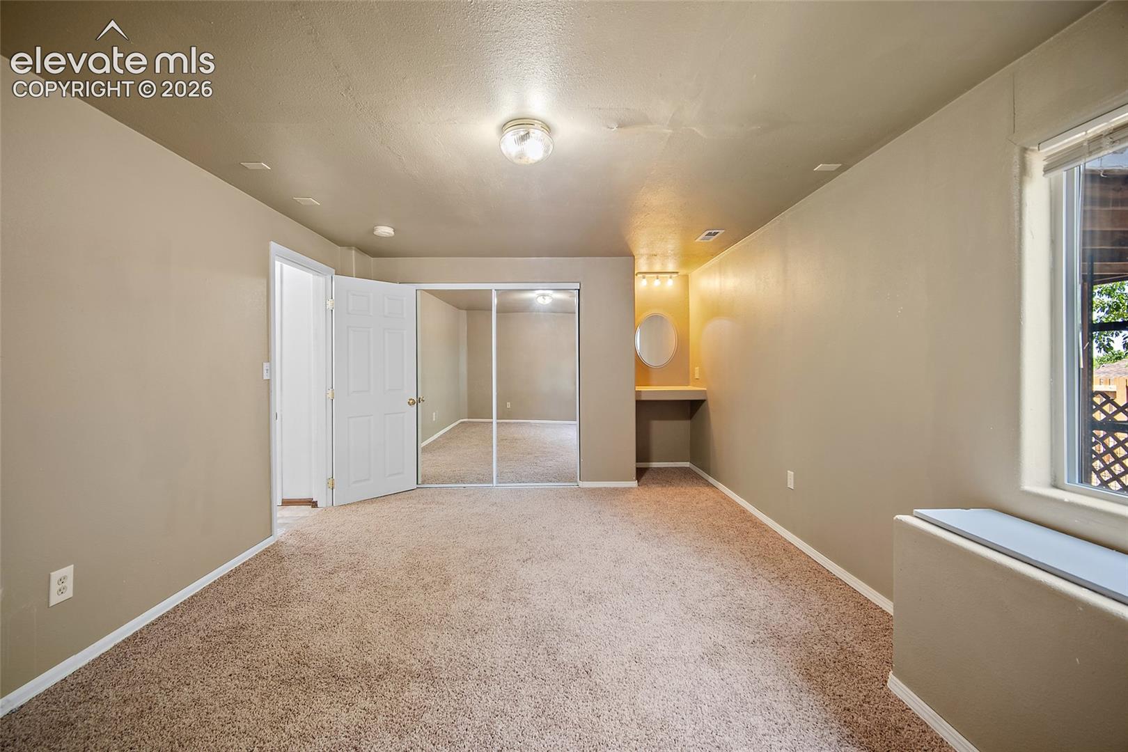 Carpeted room featuring a built-in vanity with lighting, a large window, a double-door closet with mirrored panels, and a paneled interior door