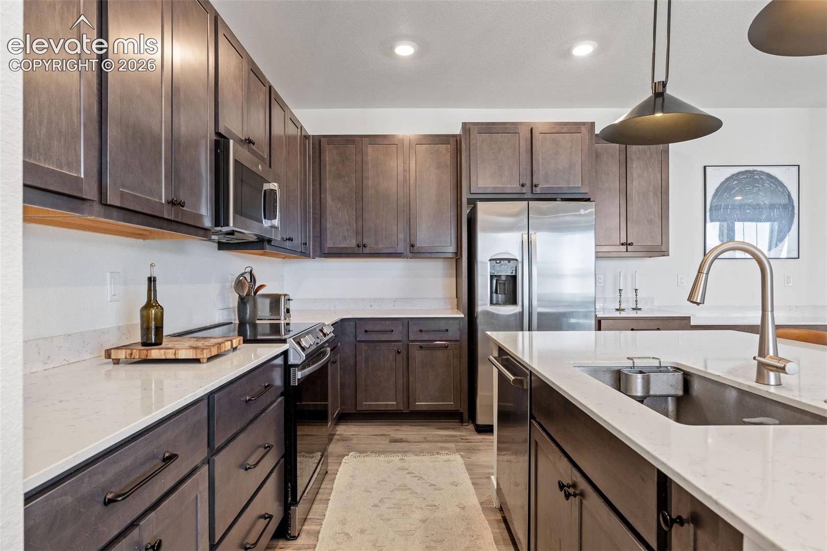 Stainless steel appliances, LVP flooring, dark wood cabinetry, white countertops, and recessed lighting