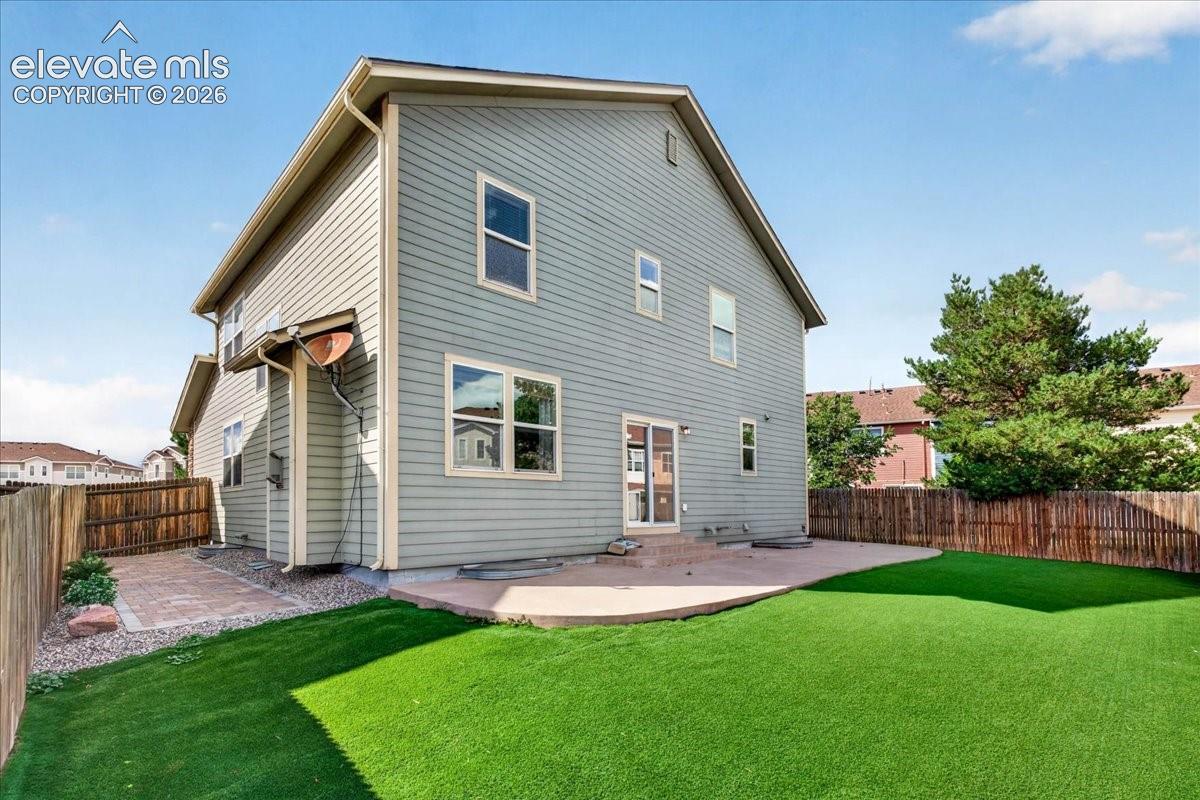 Expansive backyard featuring artificial turf, a concrete patio, and a privacy fence