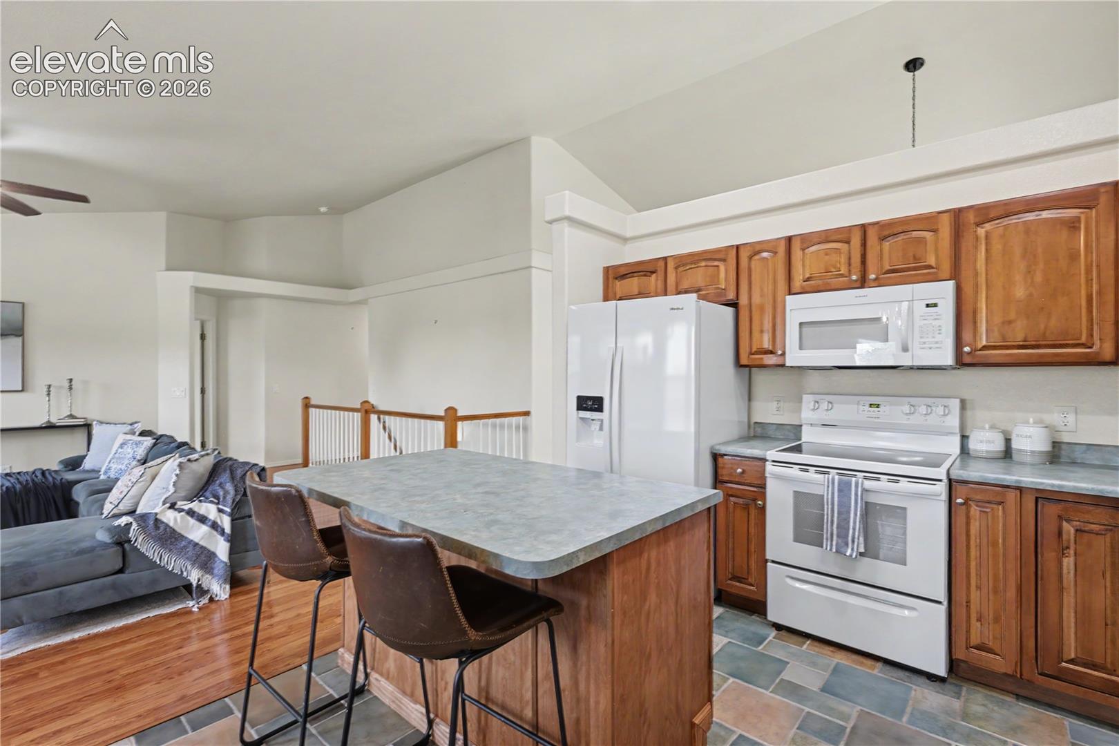 Kitchen featuring wood cabinetry, white appliances, a peninsula island with seating, and slate tile flooring