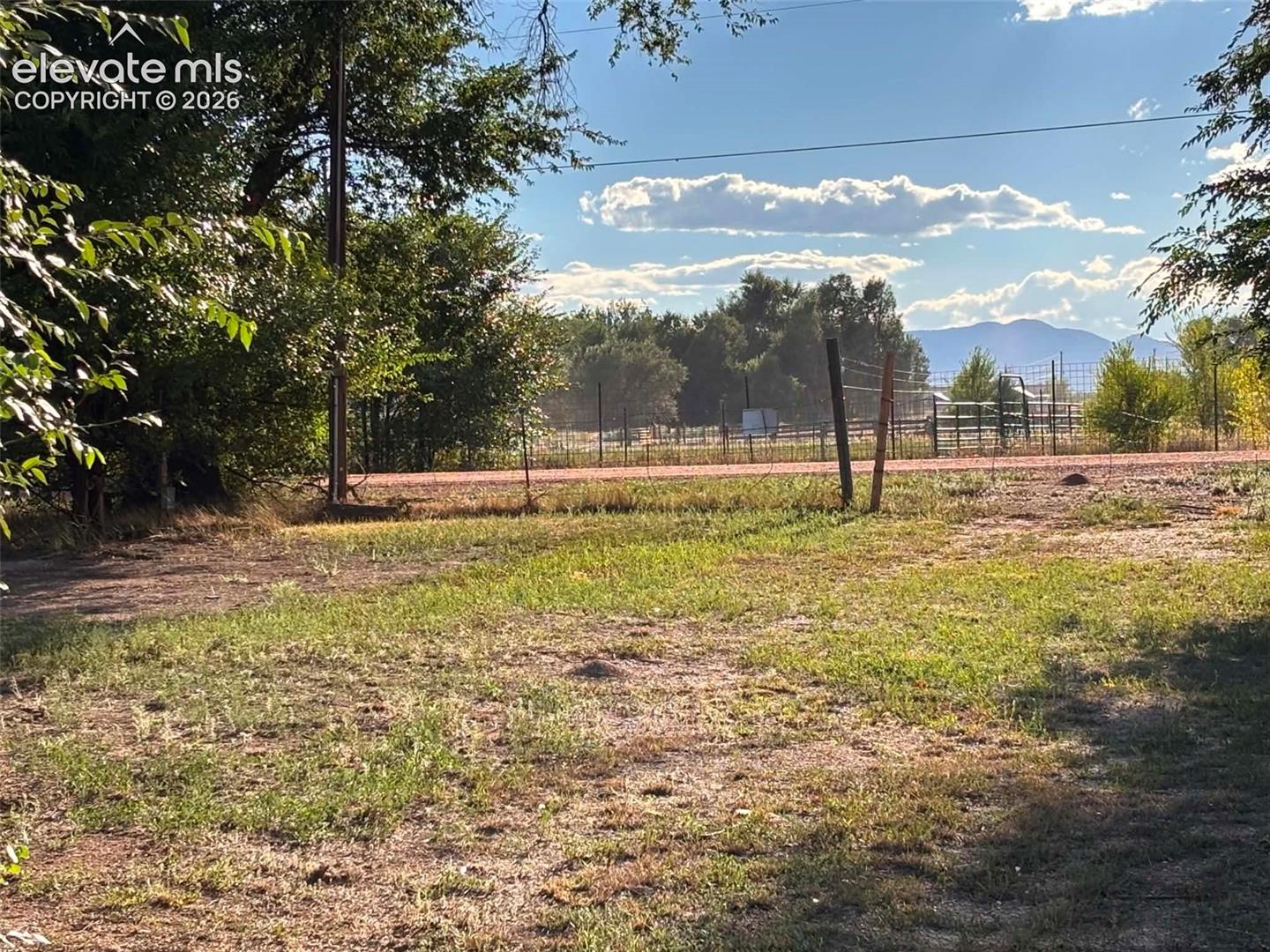 Expansive grounds featuring mature trees, wire fencing, and mountain terrain in the distance