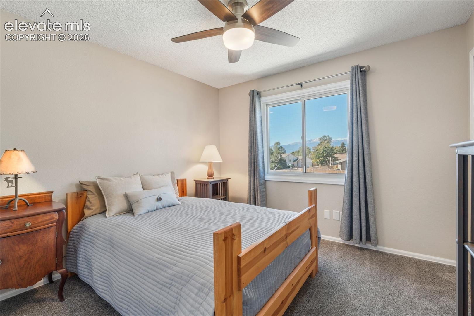 Neutral-toned room featuring a ceiling fan with integrated lighting, a sliding window with mountain scenery, and wall-to-wall carpeting