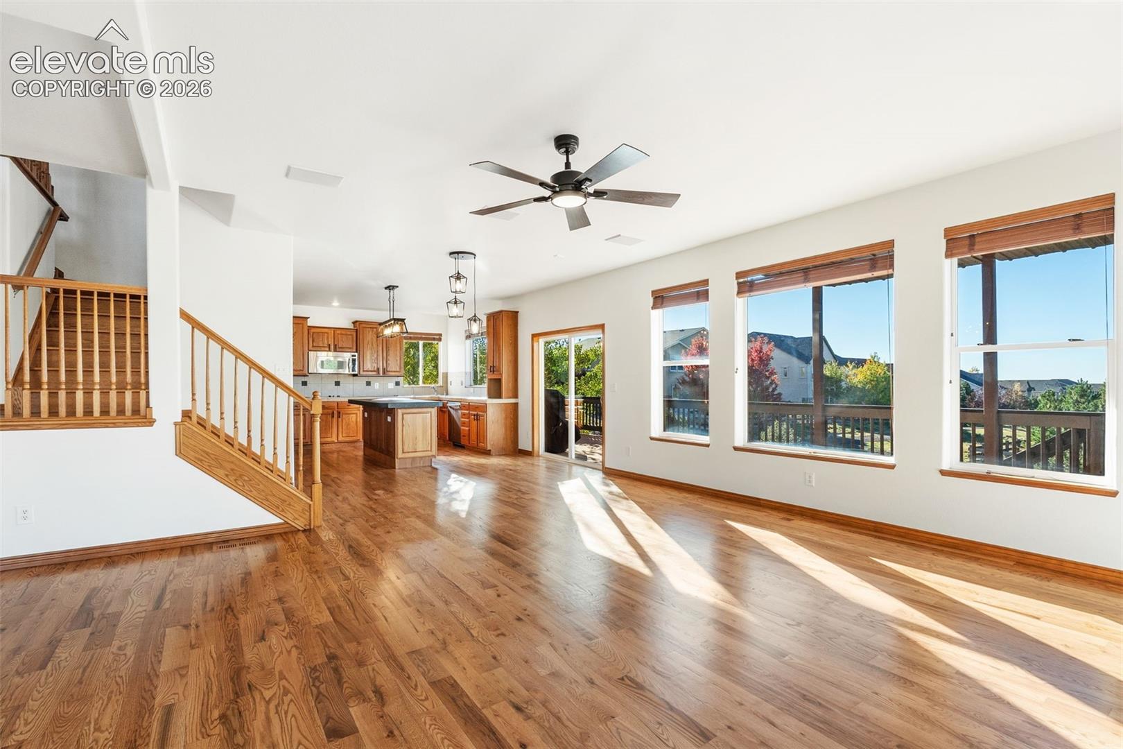 Open-concept interior featuring wood-finish flooring, staircase with wooden balusters, kitchen island, and large windows providing natural light