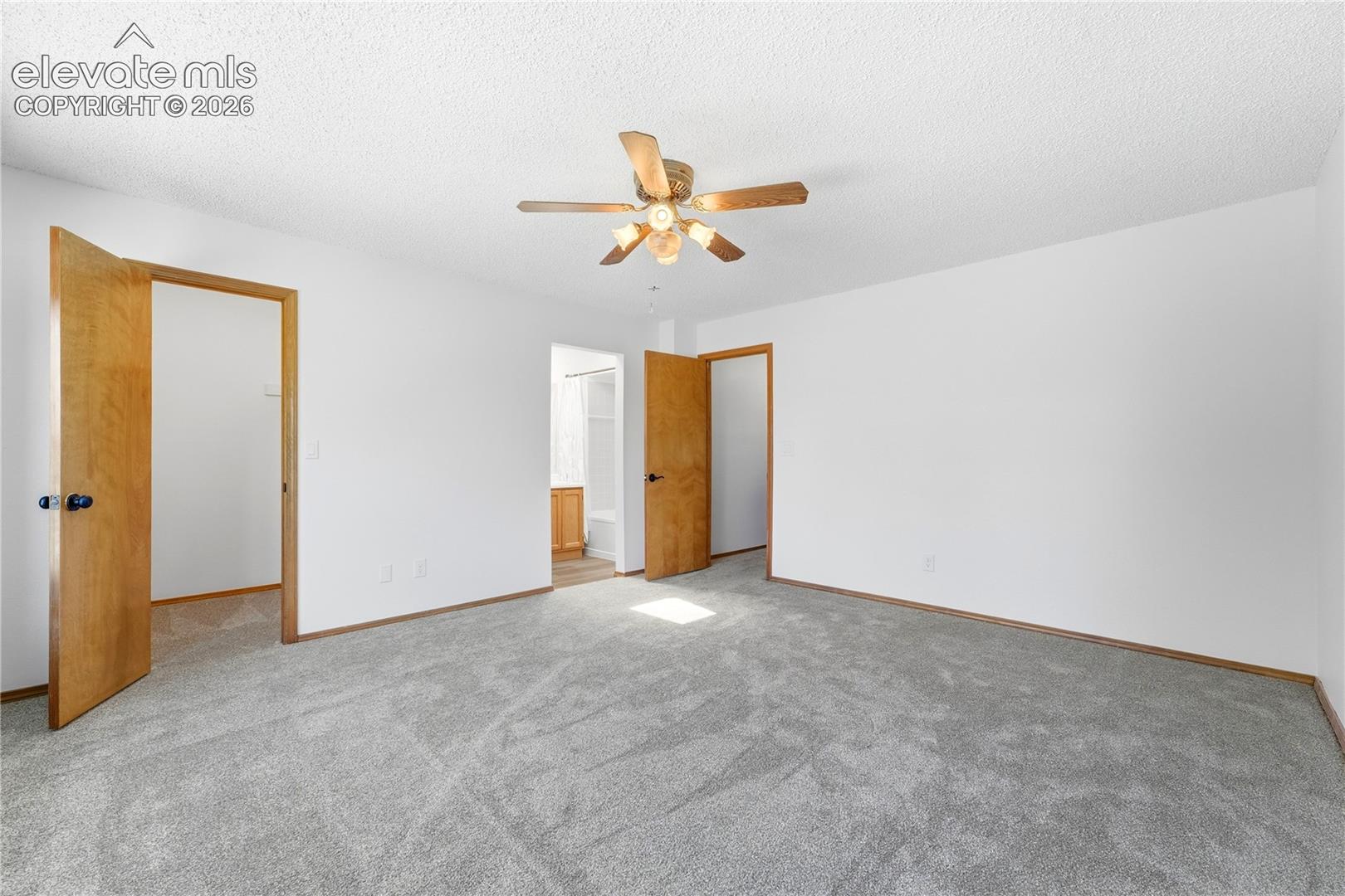 Spacious room featuring light gray carpeting, and a ceiling fan with lighting