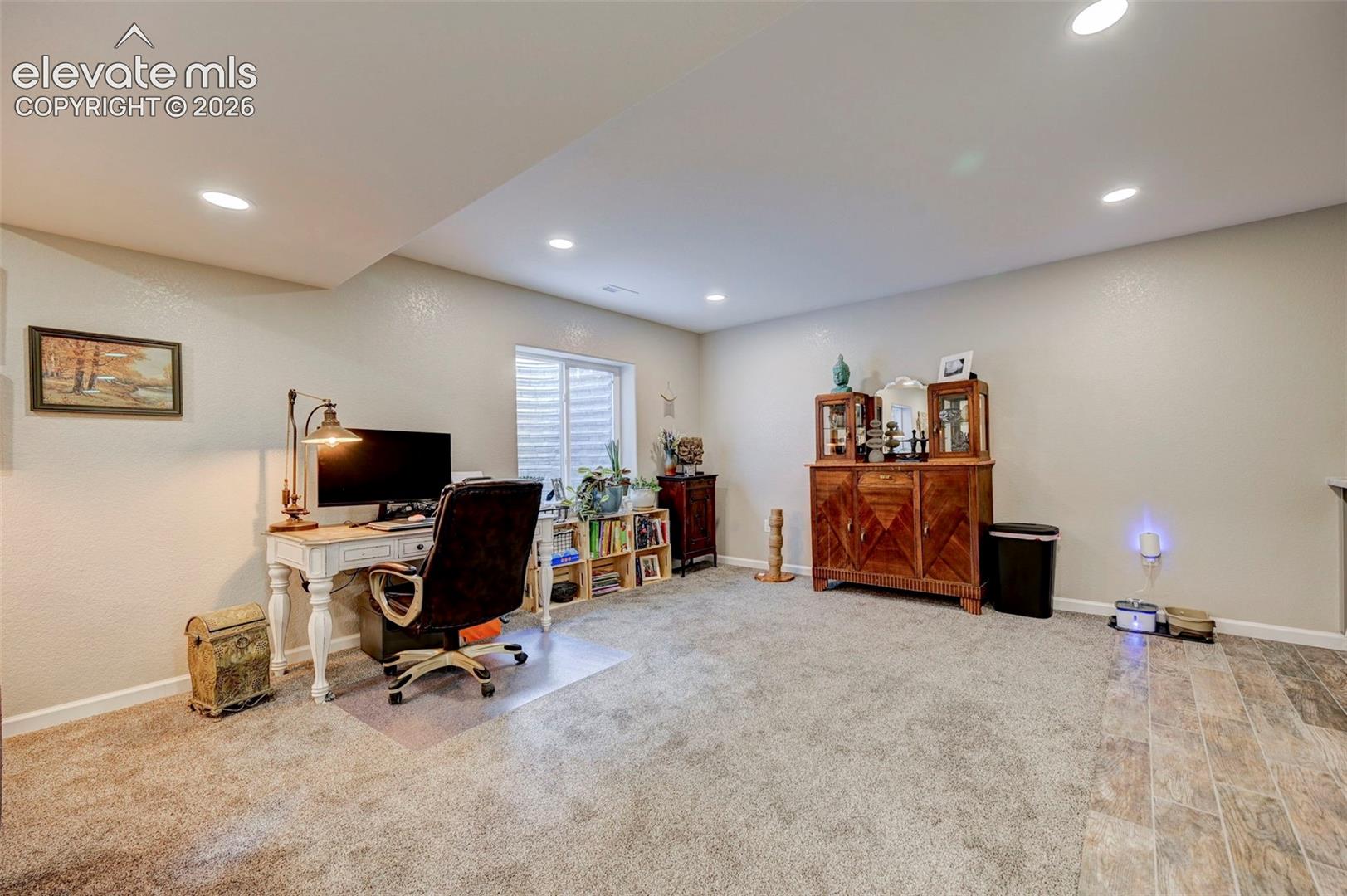 Multi-purpose room featuring recessed lighting, neutral wall tones, window with egress well, and a combination of carpet and wood-finish flooring