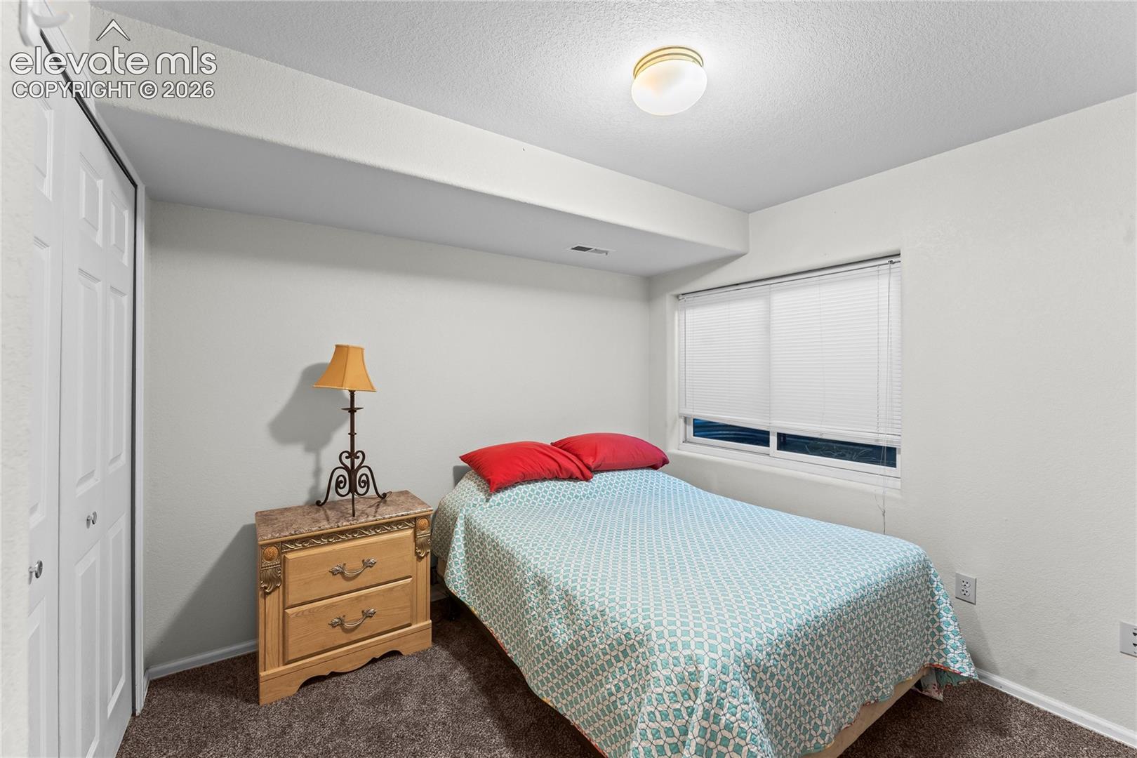 White bi-fold closet doors, wall-to-wall carpeting, and a window with blinds