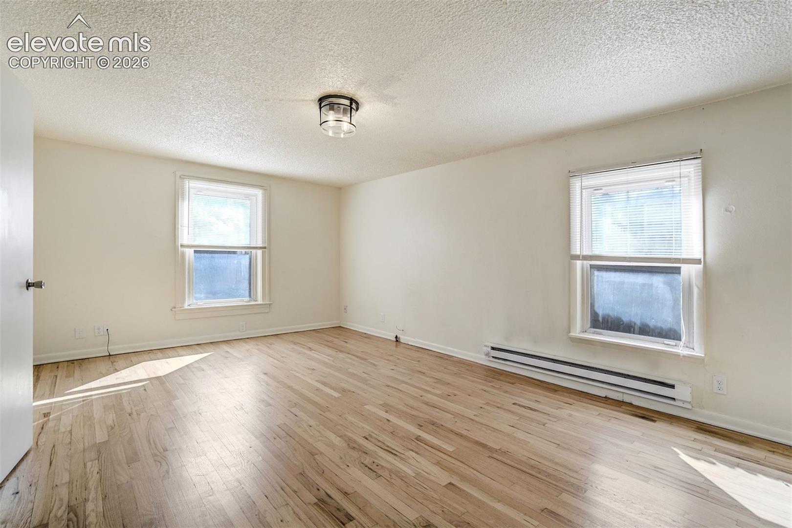 Neutral-toned room featuring wood-finish flooring, two windows with white trim, and a flush-mount ceiling light fixture