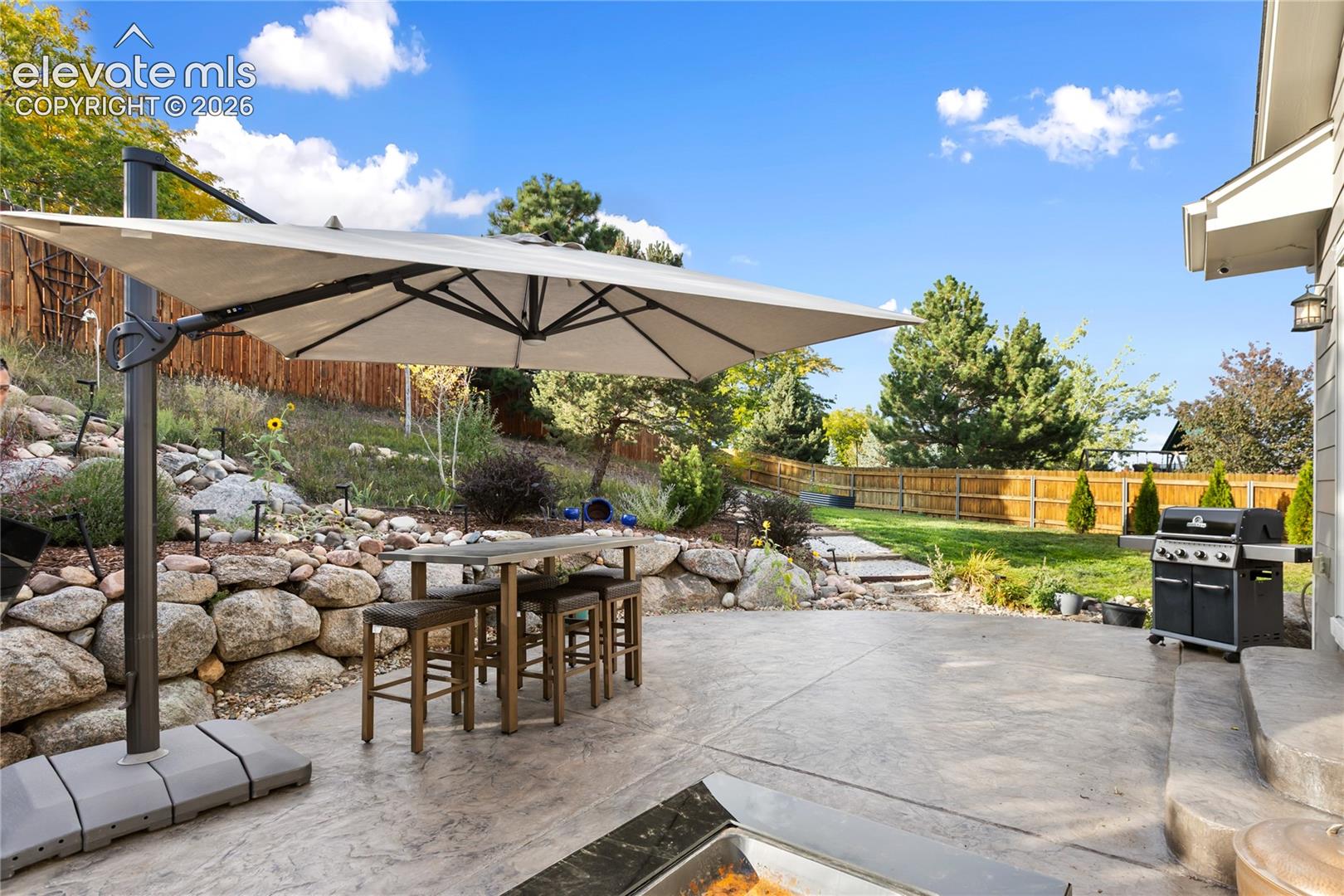 Expansive concrete patio with a stone retaining wall, terraced landscaping, and a fenced yard