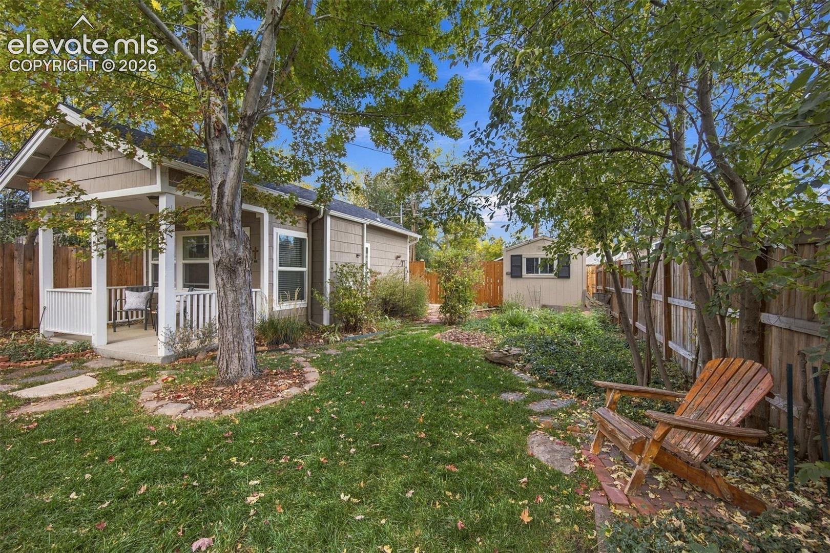 Backyard featuring a covered porch, manicured lawn, stone paver pathway, detached storage structure, and wood privacy fencing