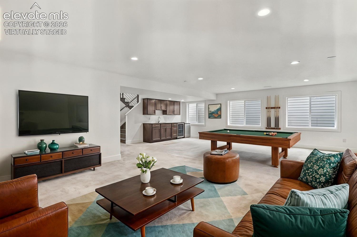 Recessed lighting illuminates the carpeted entertainment area, featuring a built-in wet bar with dark wood cabinetry and a stainless steel sink. Virtually Staged