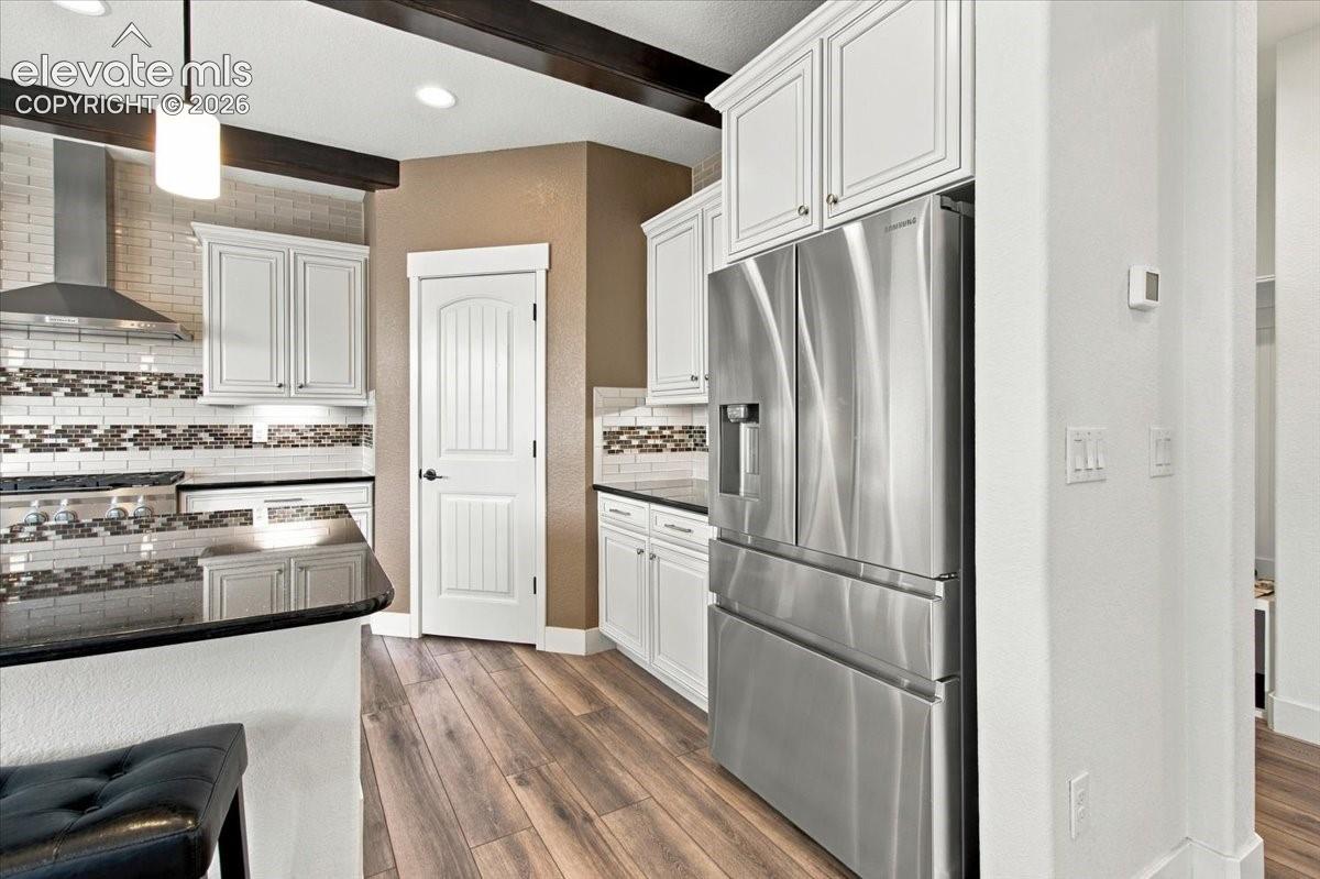 Kitchen featuring white shaker-style cabinetry, wood-finish flooring, dark stone countertops, stainless steel appliances, and ceiling beams