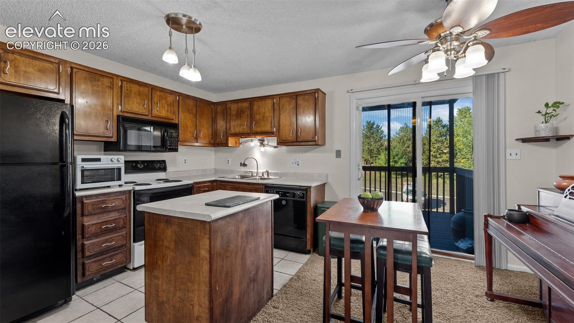 Kitchen featuring wood cabinetry, a center island with a stone-finish countertop, black appliances, tile flooring, and a sliding glass door providing exterior access