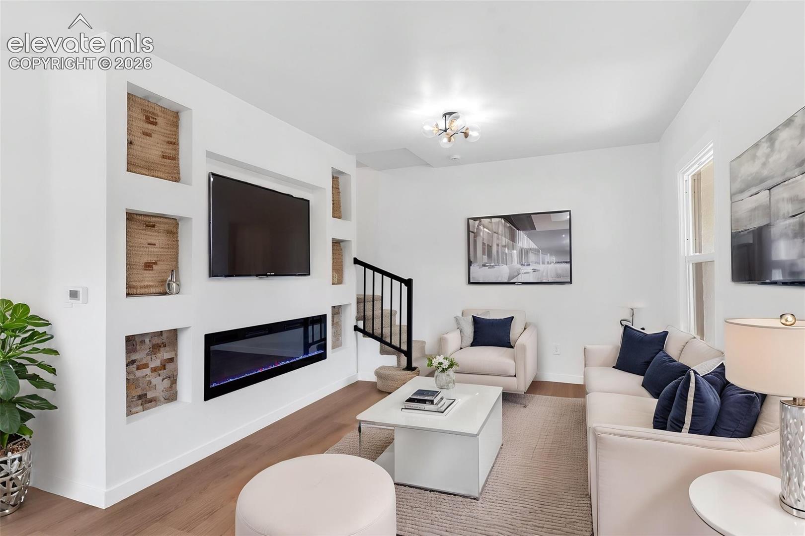 Living area featuring a custom wall unit with built-in shelving, integrated electric fireplace, wood-finish flooring, and a modern multi-bulb flush mount light fixture