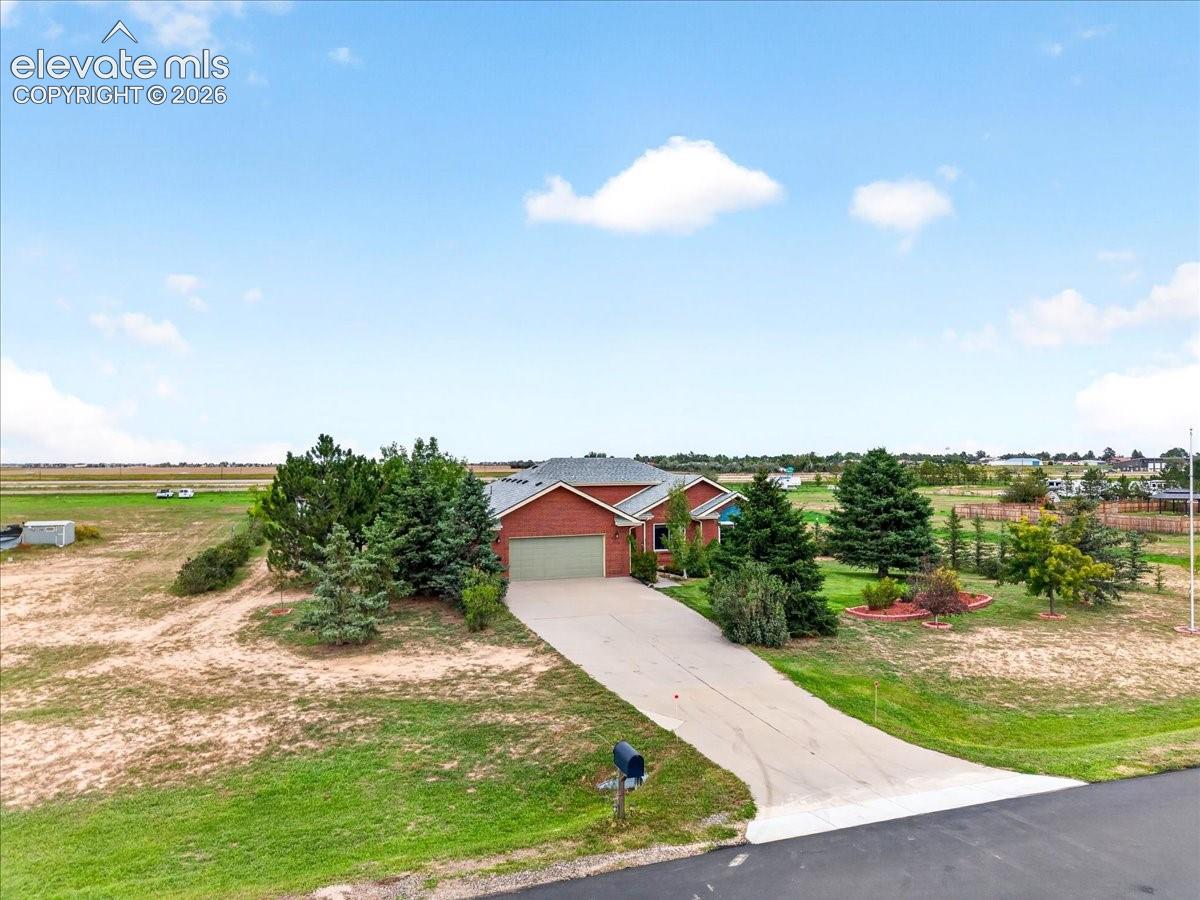 Single-story brick exterior residence featuring a gabled roofline, an attached two-car garage, and a concrete driveway situated on an expansive lot with mature landscaping