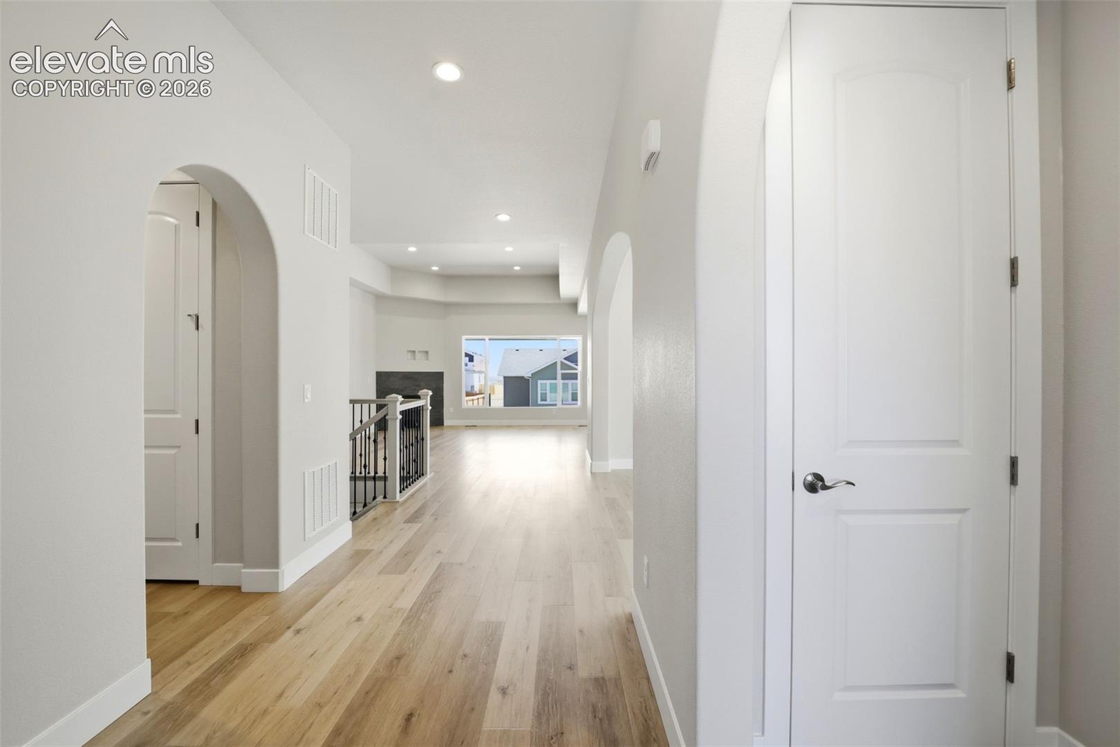 Interior hallway featuring arched architectural entryways, wood-finish flooring, recessed lighting, and a tiered tray ceiling