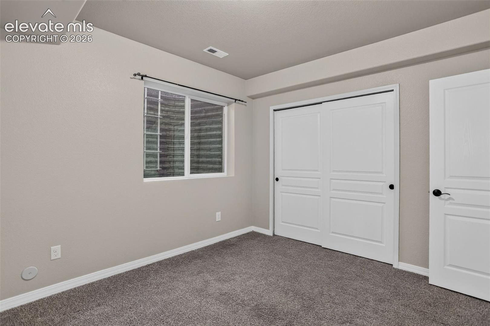 Neutral wall paint, gray carpet, white trim, sliding closet doors with black hardware, and an egress window