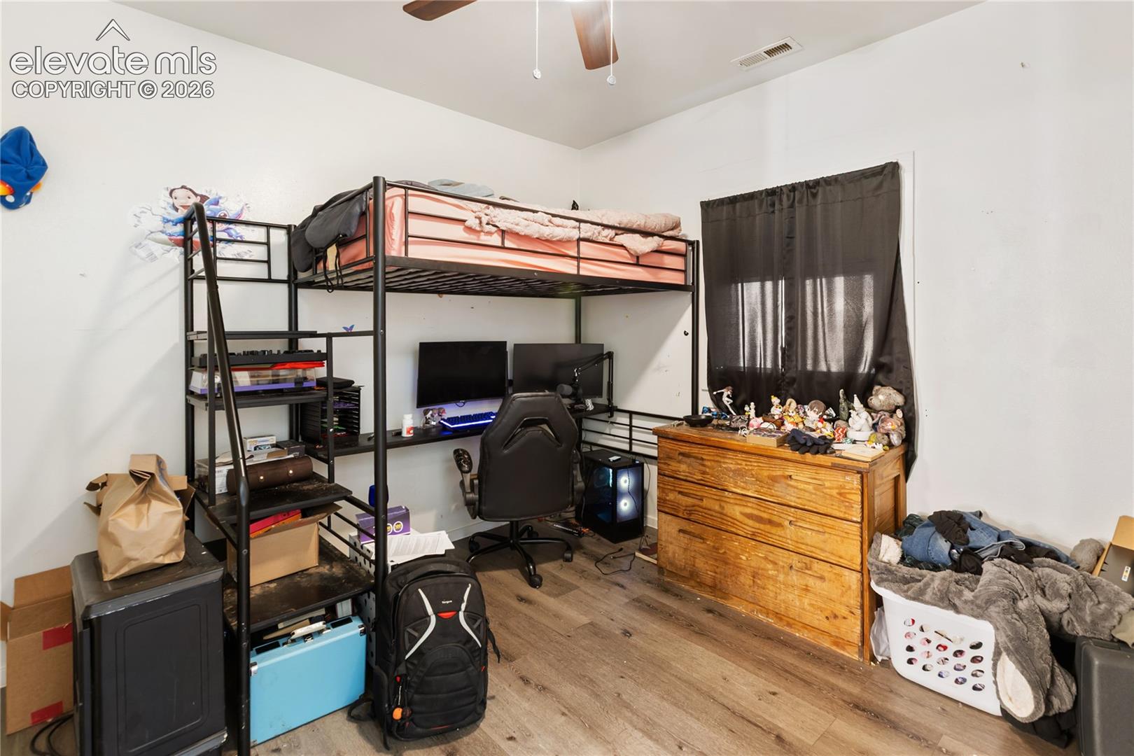 Room featuring wood-finish flooring, a ceiling fan with light fixture, and a window with trim