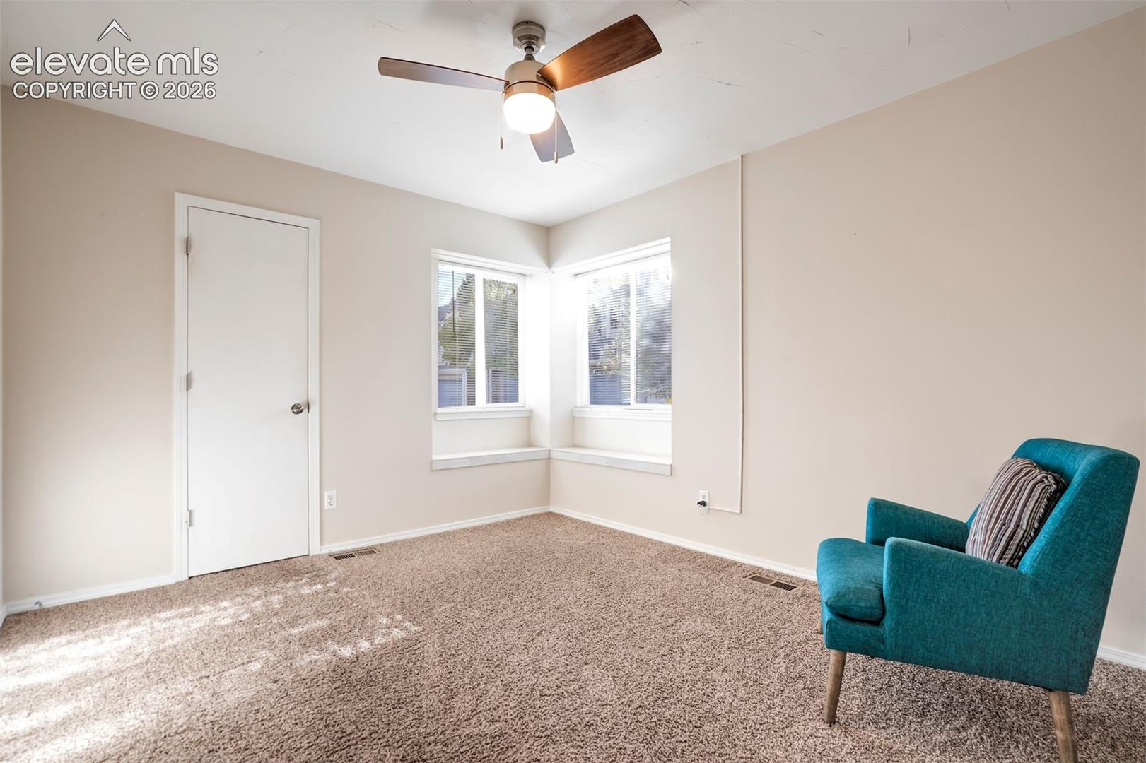 Room featuring neutral wall tones, wall-to-wall carpeting, a corner window configuration with built-in ledges, and a ceiling fan with integrated lighting