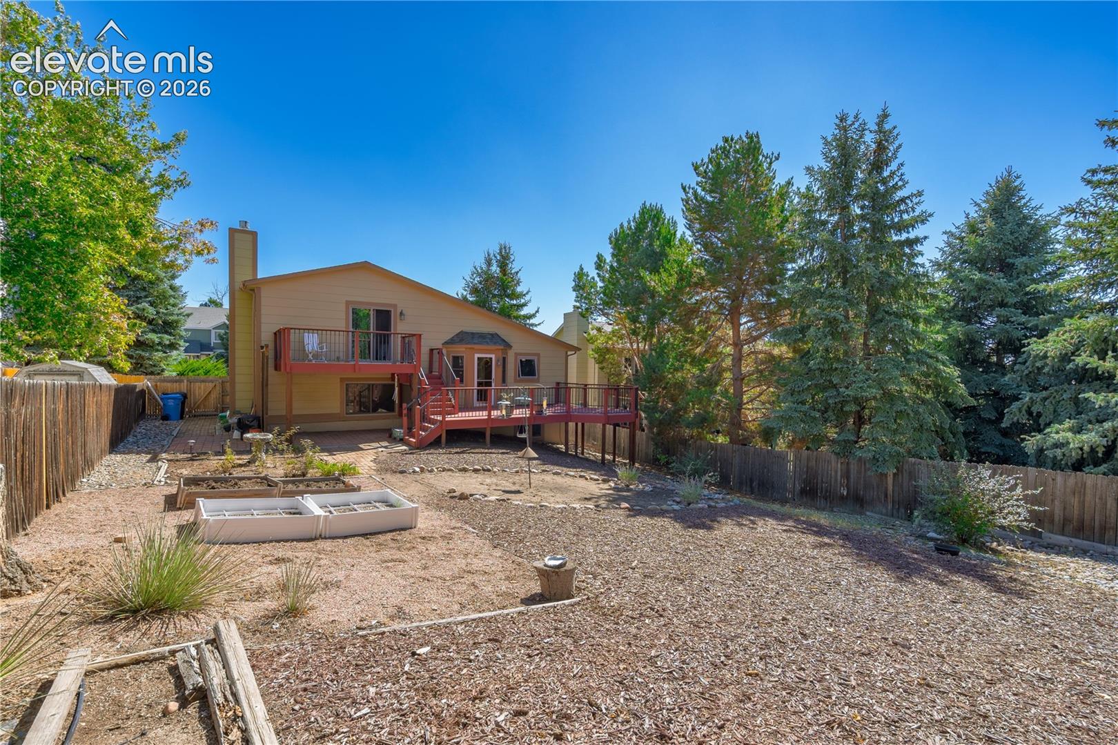 Fenced backyard with multi-level wood deck, established trees, and raised planting beds