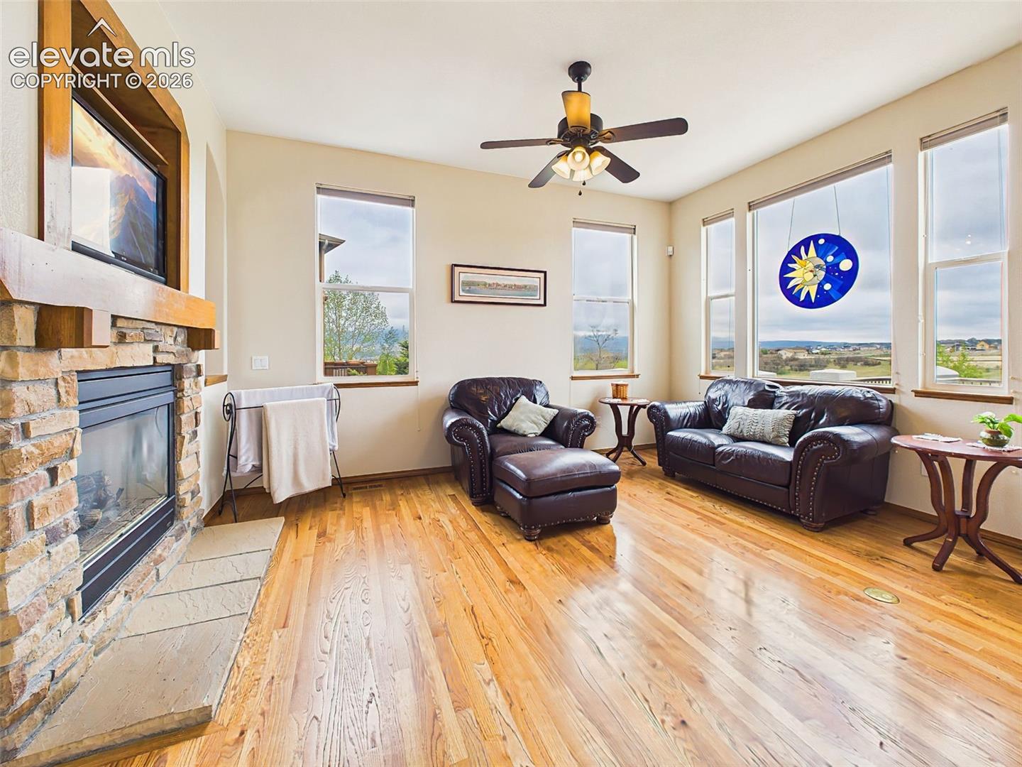 Comfortable living room featuring a floor-to-ceiling stone fireplace, ceiling fan, and large windows overlooking the Front range and open space
