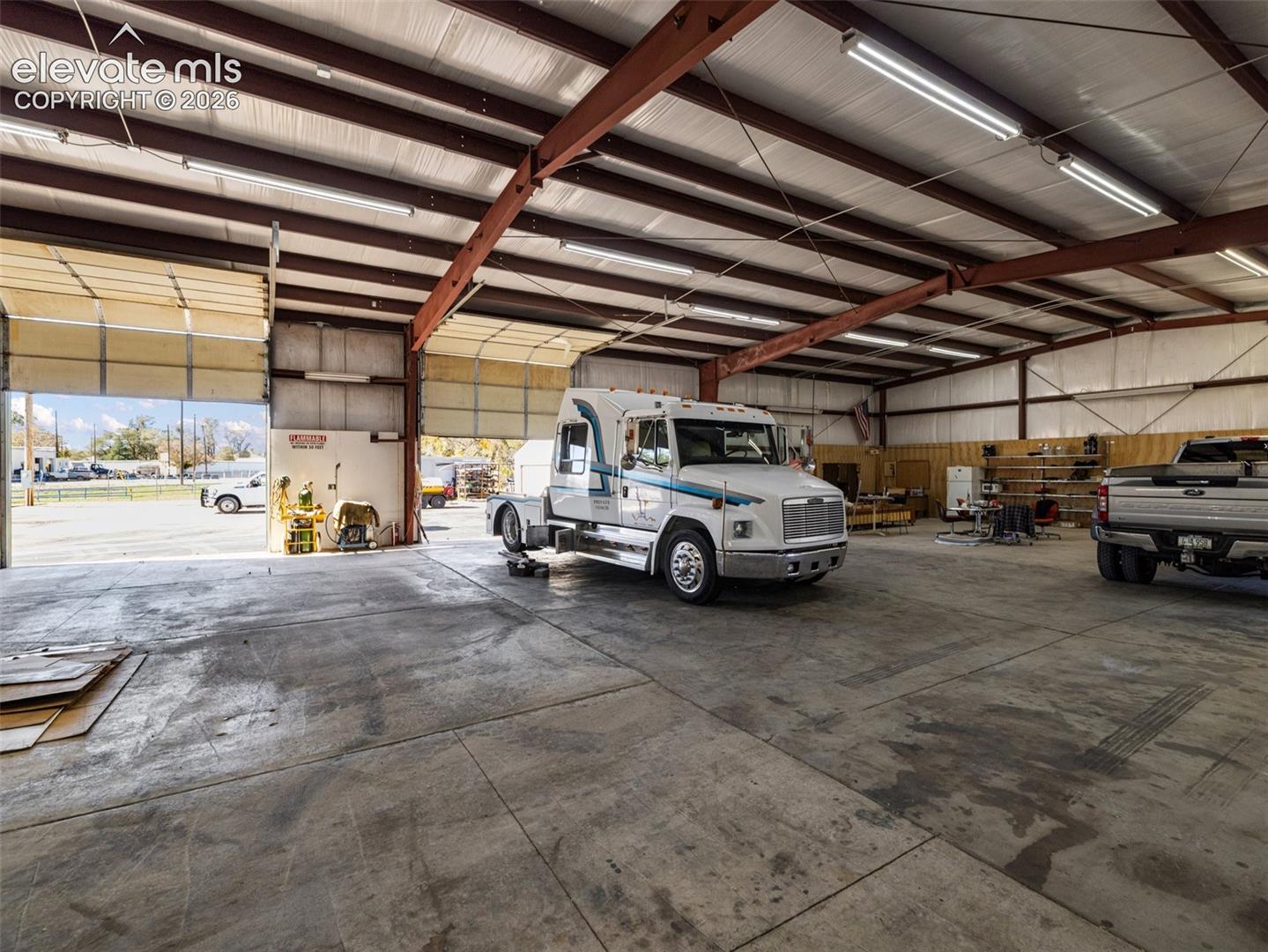 Industrial warehouse featuring exposed steel framing, concrete flooring, multiple overhead doors, and high-intensity linear lighting