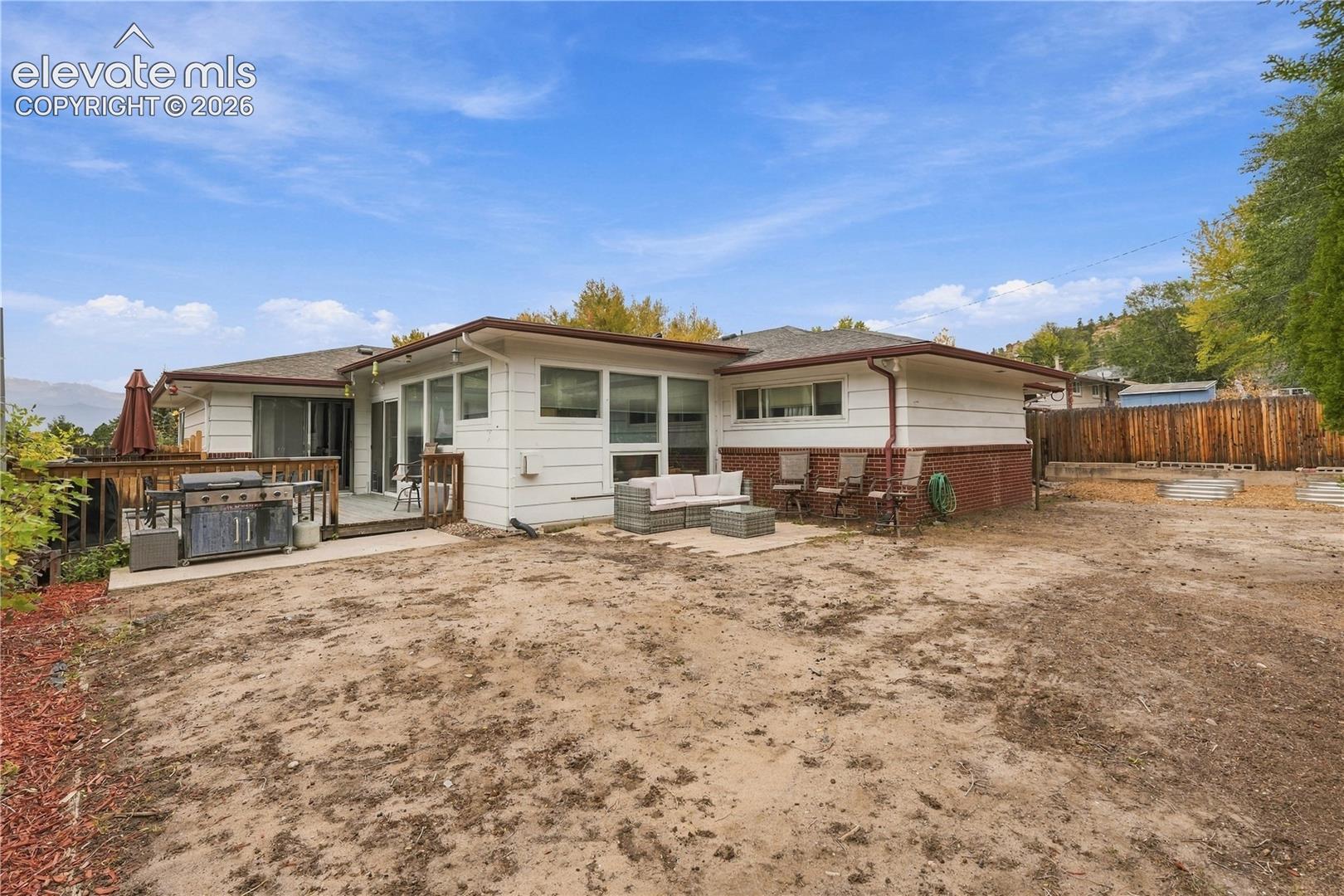 Exterior featuring horizontal siding, brick masonry foundation, raised wood deck, and concrete patio
