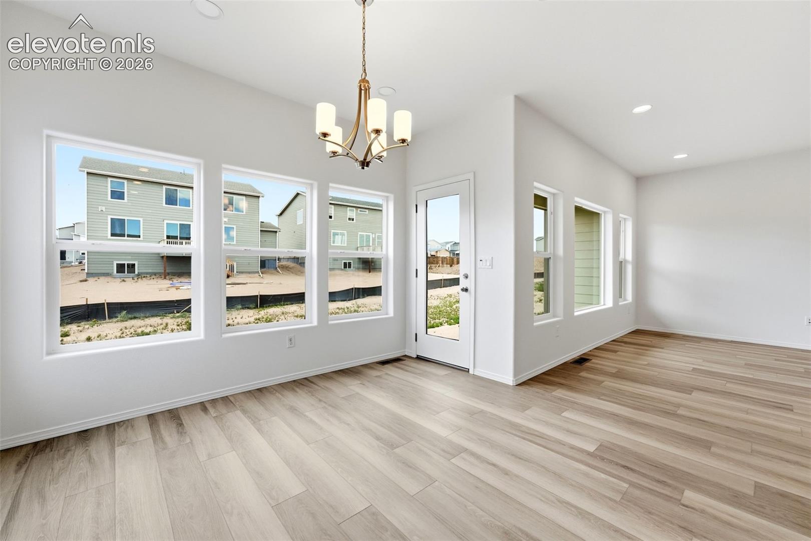 Bright room featuring wood-finish flooring, numerous windows, a multi-light chandelier, recessed lighting, and a glass-paneled exterior door