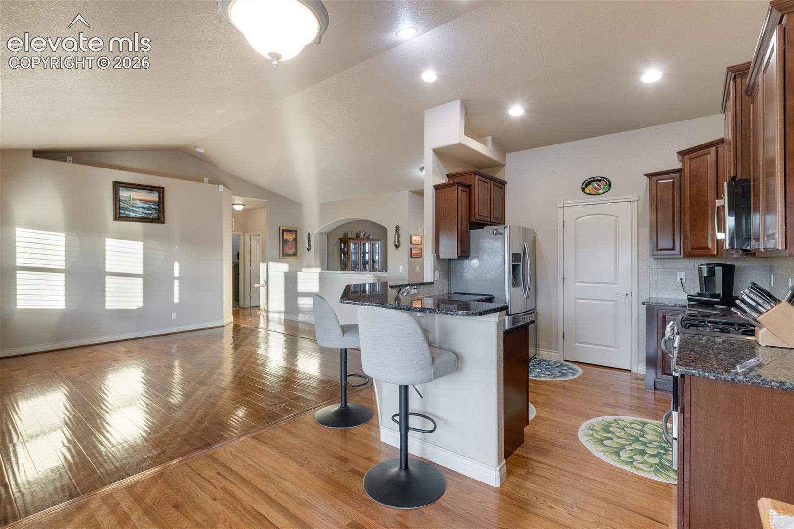 Kitchen featuring dark wood cabinetry, stone-surface countertops, a breakfast bar, recessed ceiling lighting, and wood-finish flooring, large pantry in the background