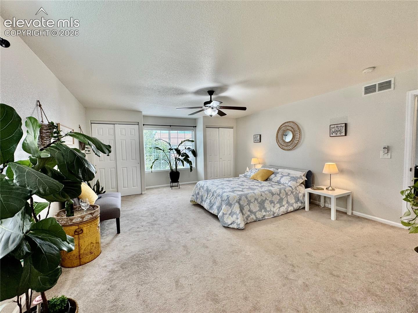 Spacious carpeted room featuring a ceiling fan, multiple windows, and two sets of bi-fold closet doors