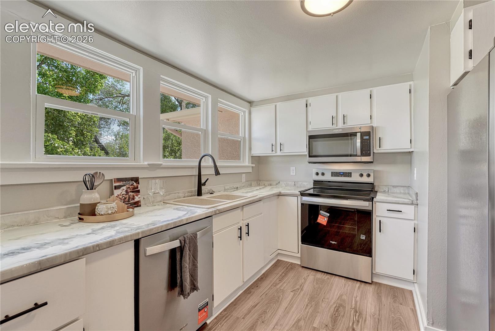 Kitchen featuring white cabinetry, light-toned countertops, wood-finish flooring, stainless steel appliances, and a double basin sink
