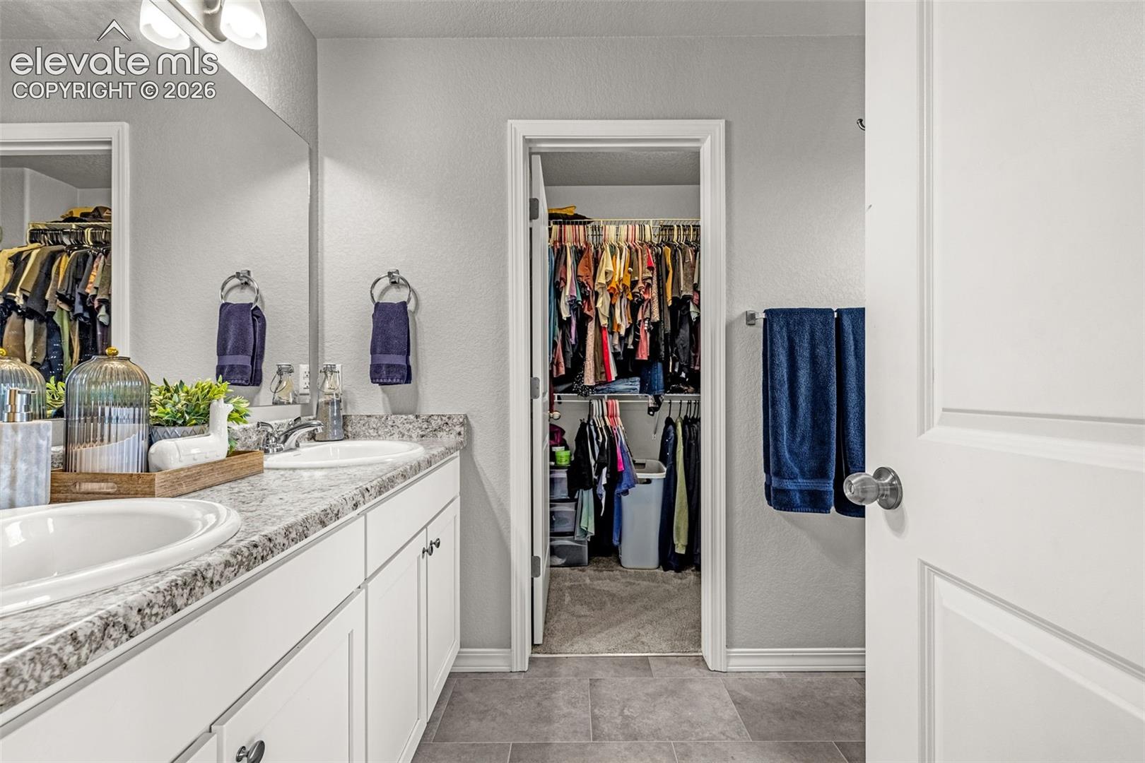 Bathroom featuring a dual vanity with undermount sinks, speckled countertop, and white cabinetry