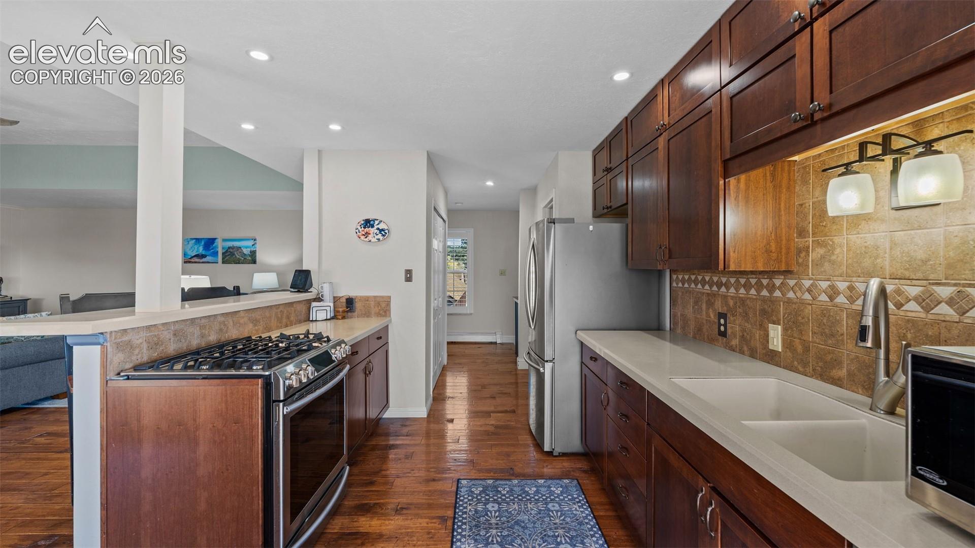 Kitchen featuring dark wood cabinetry, quartz countertops, a dual-basin undermount sink, a stainless steel gas range, and recessed lighting