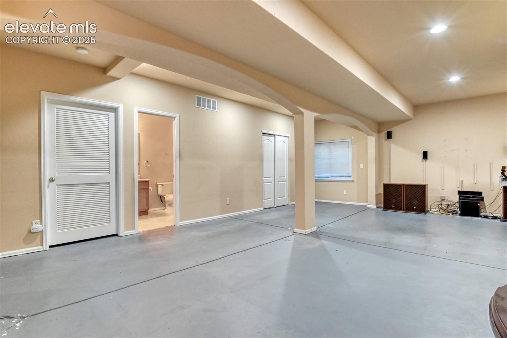 Finished interior space featuring arched structural beams, painted concrete flooring, louvered closet doors, and recessed ceiling lighting