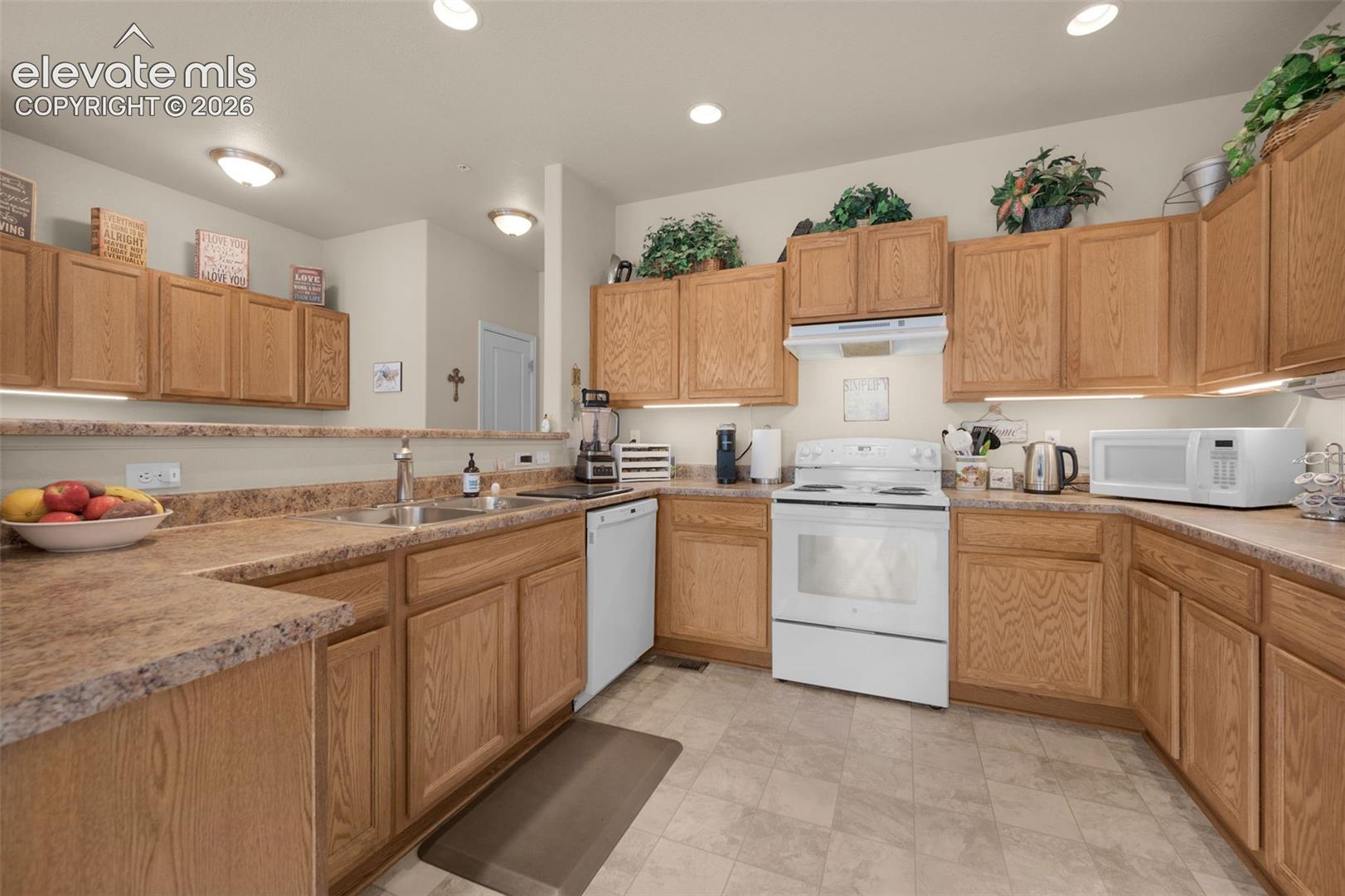 Kitchen featuring light wood cabinetry, stone-look laminate countertops, and a white oven with an overhead vent fan