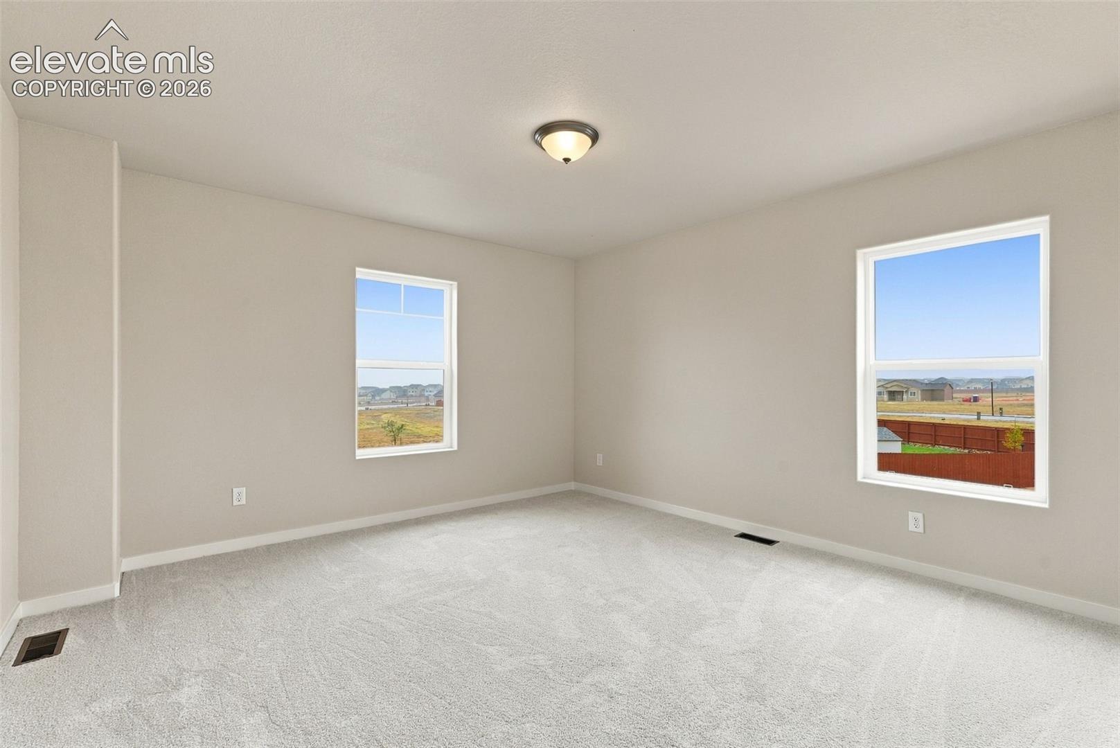 Neutral-toned interior space featuring light-colored wall-to-wall carpeting, dual windows, and a flush-mount ceiling light fixture