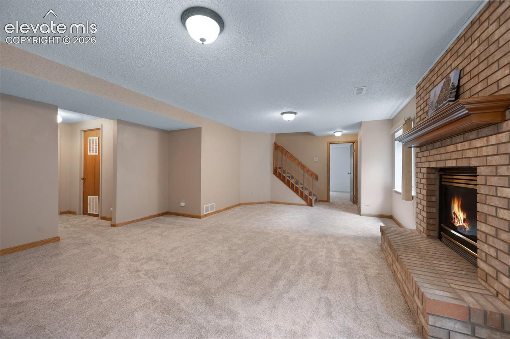 Unfurnished living room with a fireplace, stairway, a textured ceiling, light carpet, and baseboards. fireplace staged and added.