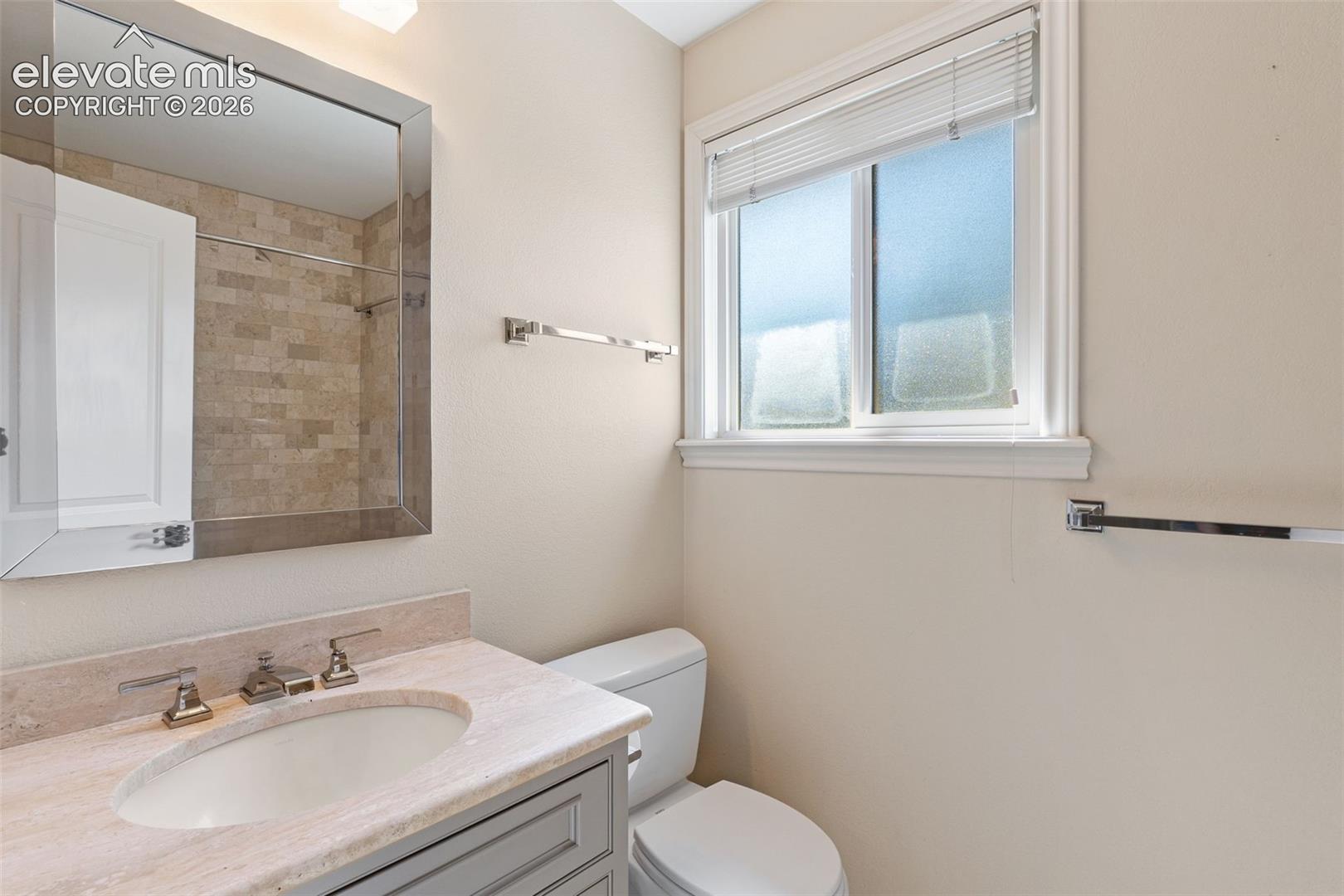 Bathroom featuring a vanity with a stone countertop, an integrated oval basin, framed mirror, and horizontal window with privacy glass