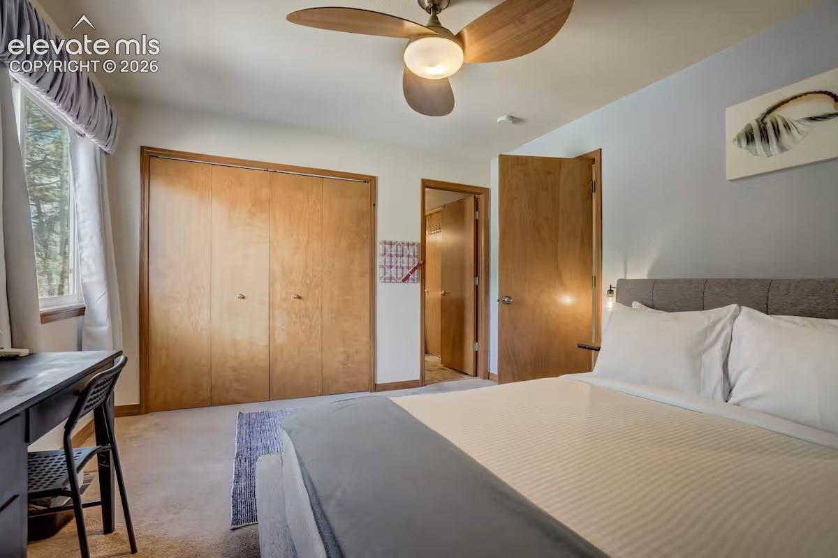 Room featuring light-colored carpet flooring, a window with drapery, wood-finish closet doors, and an overhead ceiling fan with light