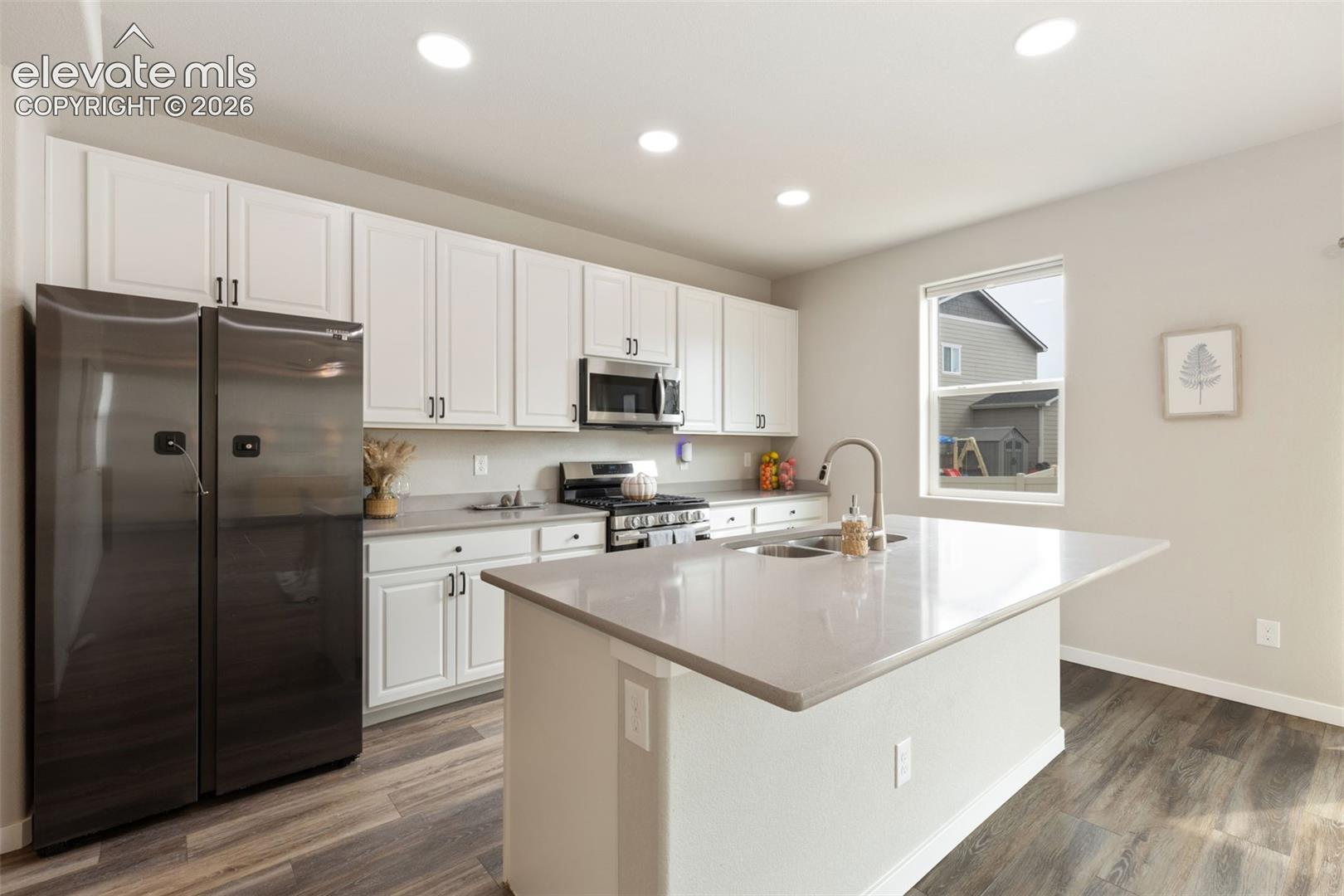 Modern kitchen featuring white cabinetry, stainless steel appliances, gas stove, a center island with an integrated sink, and wood-finish flooring